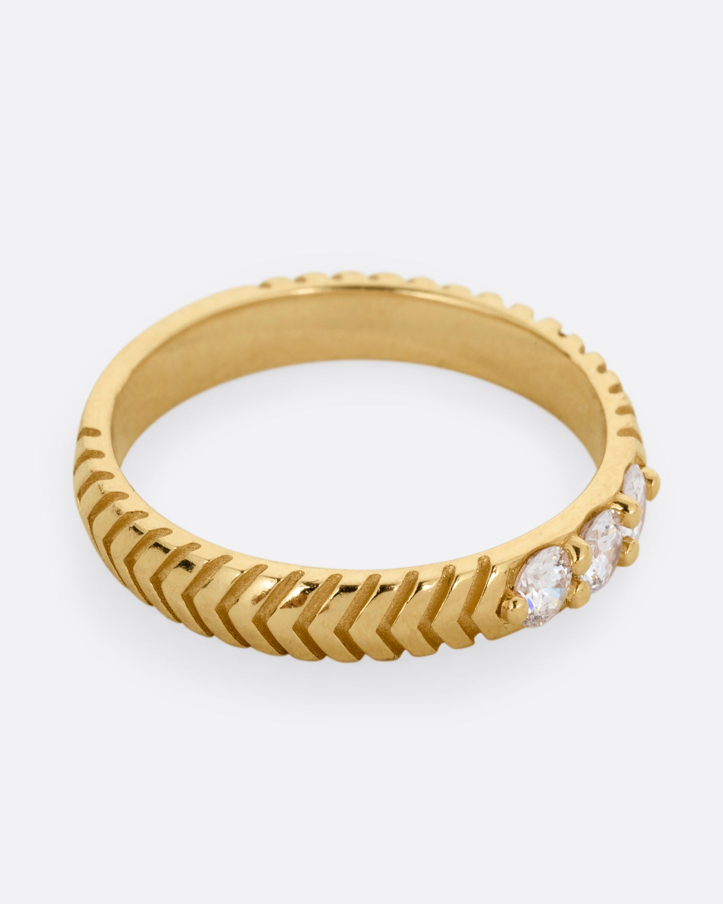 A yellow gold ring with arrow etching and three white diamonds. Shown from the side.