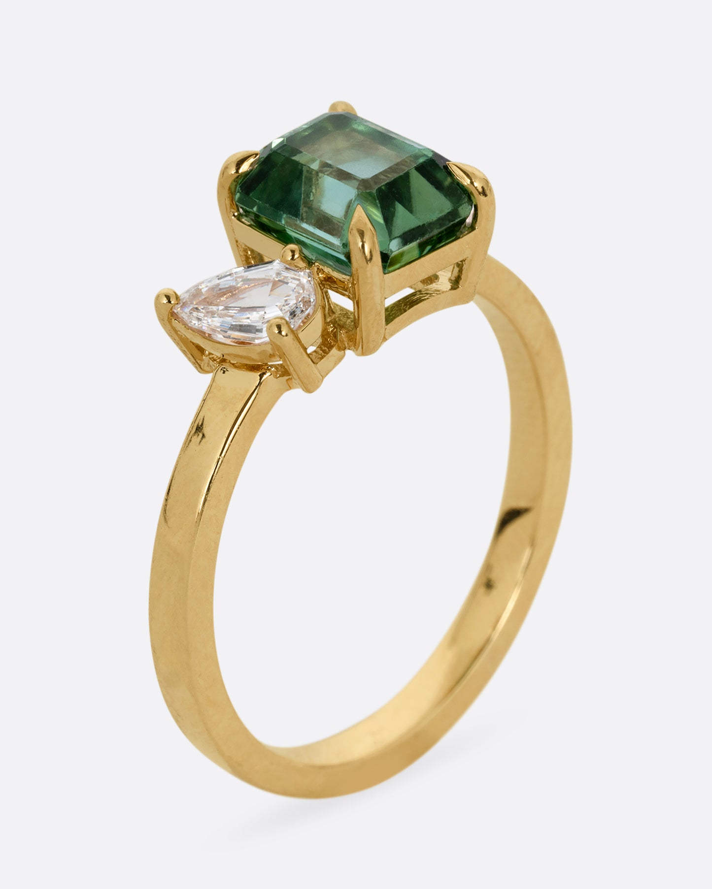 A yellow gold ring with a green tourmaline and pear cut diamond, shown standing up from the side.