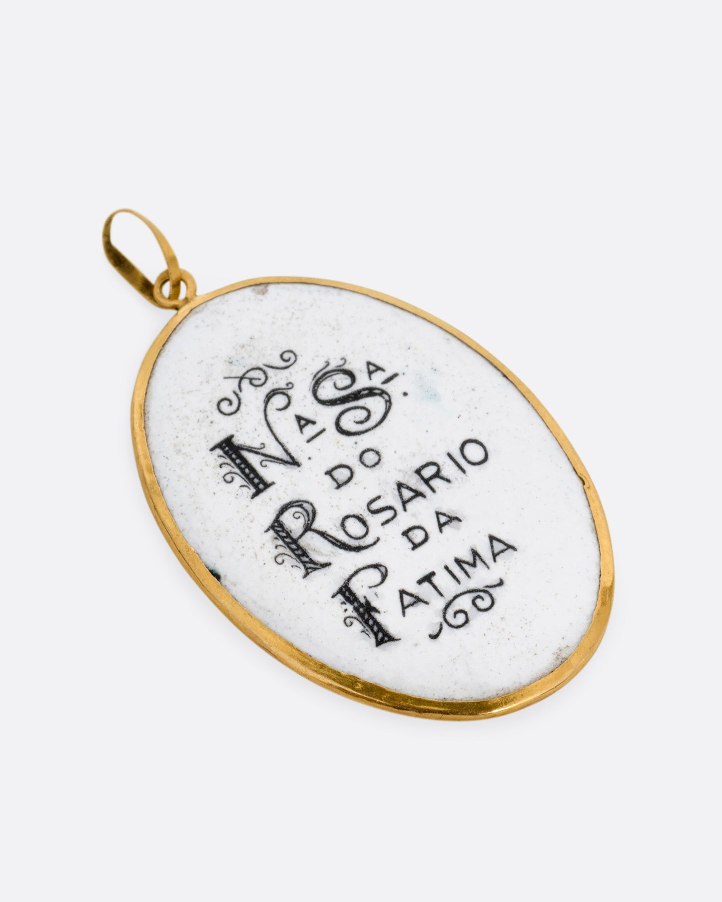 A yellow gold pendant with a hand painted image of the Virgin Mary sits at the center and "Na sa do Rosario da Patima" on its reverse. Shown from the back.