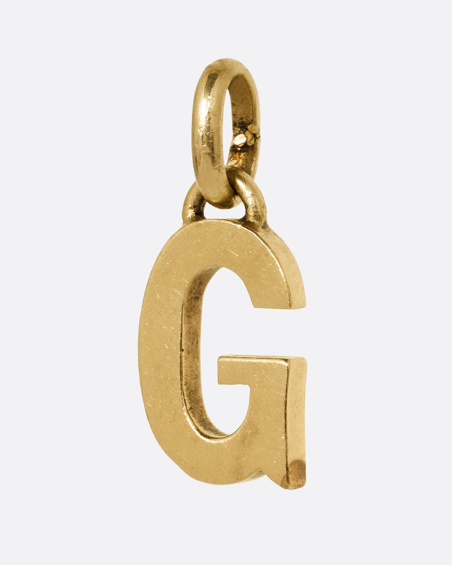 A yellow gold letter 'G' pendant shown from the side.