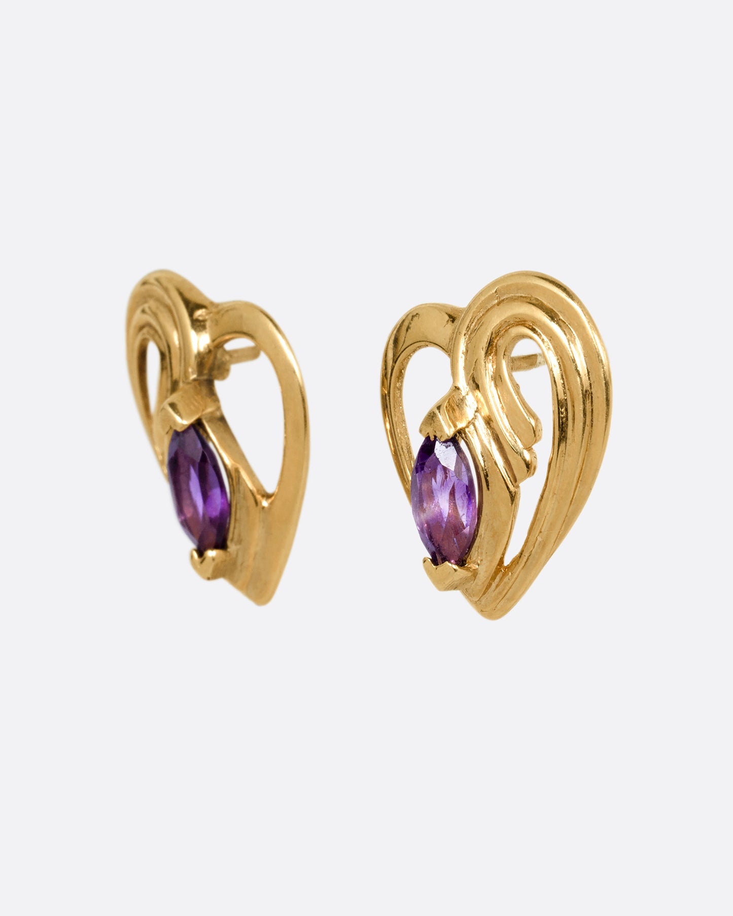 A pair of yellow gold heart shaped stud earrings with marquise amethysts at the center. Shown from the side.