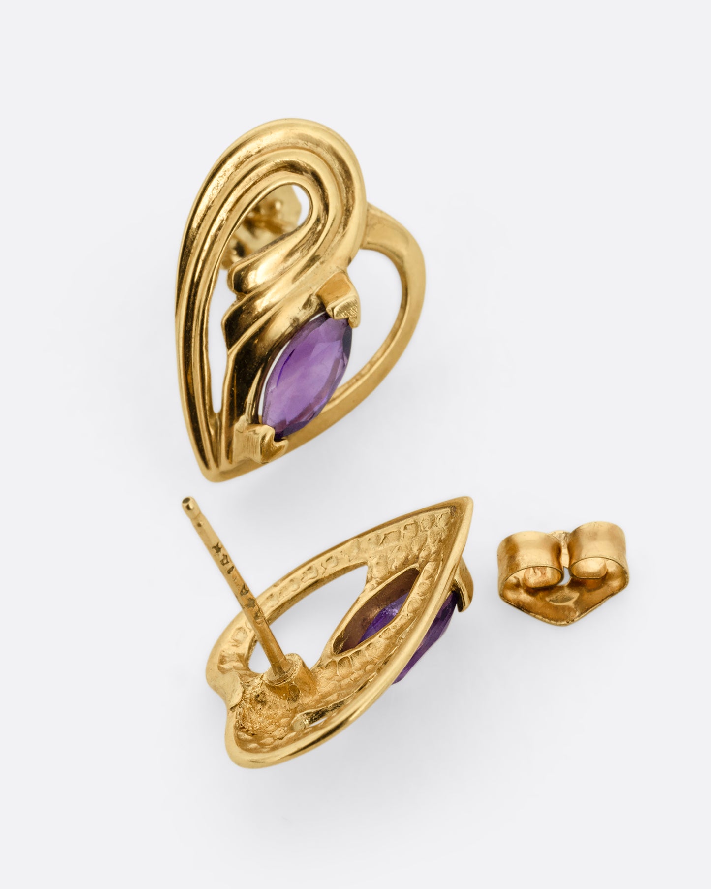 A pair of yellow gold heart shaped stud earrings with marquise amethysts at the center. One earring is shown from the front, the other open from the back.