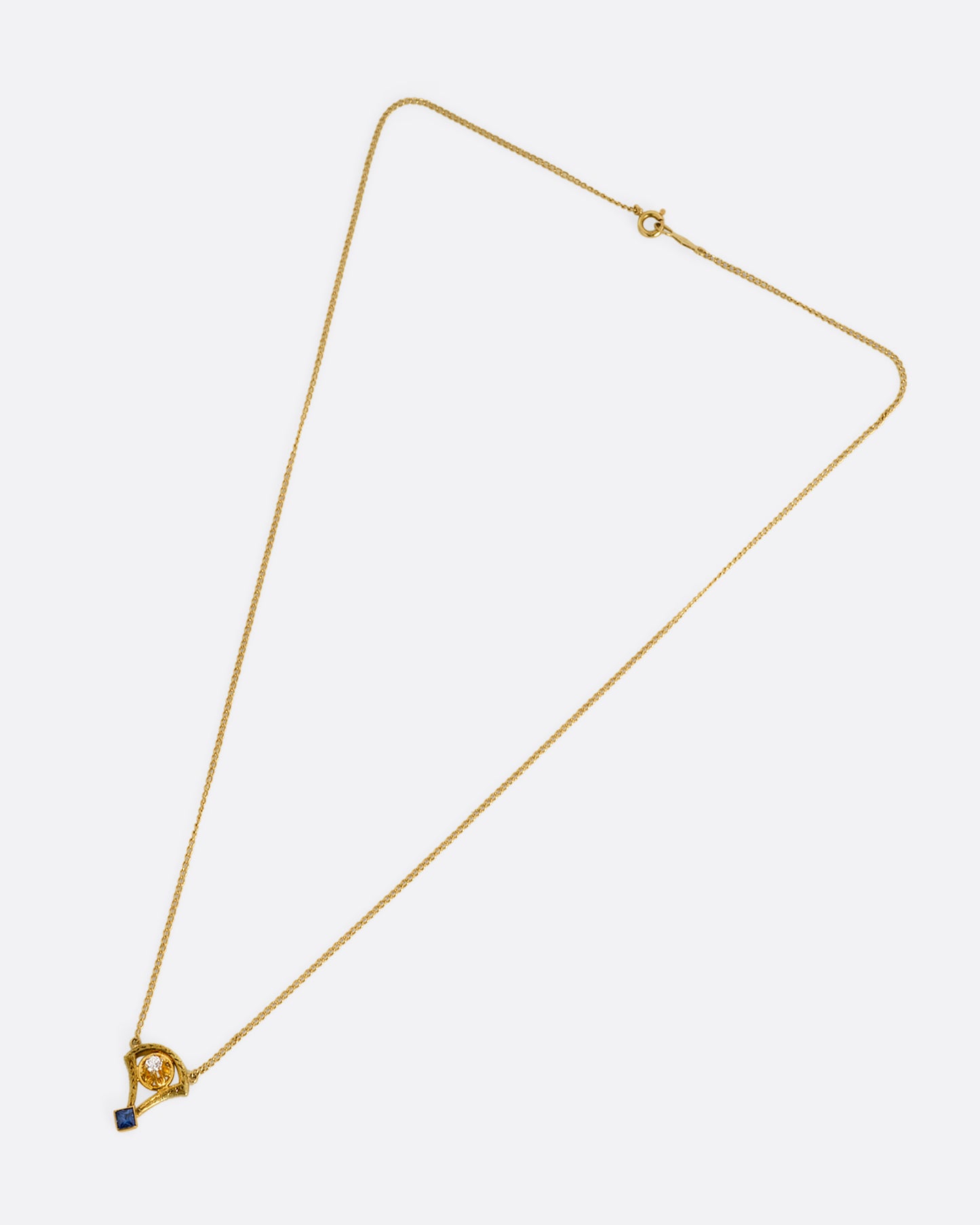 A yellow gold cable chain necklace with a pendant shaped like the basket of a mini hot air balloon with a prong set diamond. and princess cut sapphire. Shown from the front.