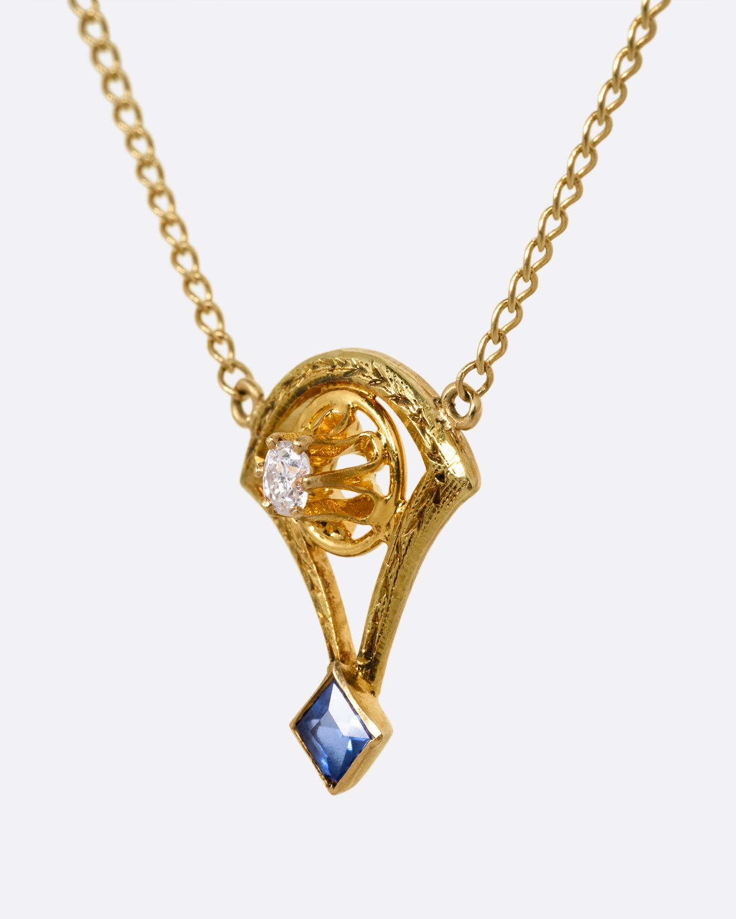 A yellow gold cable chain necklace with a pendant shaped like the basket of a mini hot air balloon with a prong set diamond. and princess cut sapphire. Shown from the side.