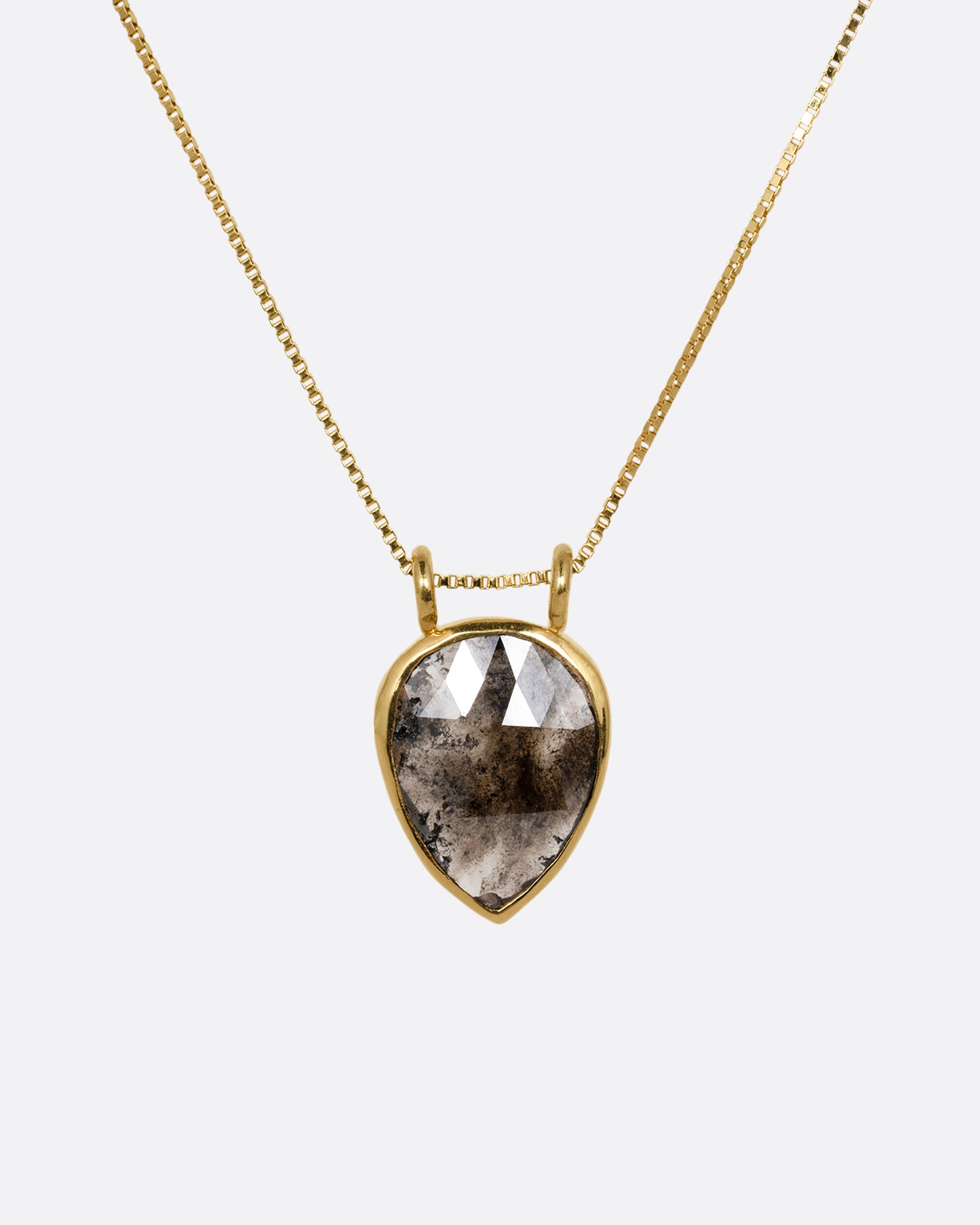 A yellow gold box chain necklace with a pear shaped salt and pepper diamond pendant shown from the front.