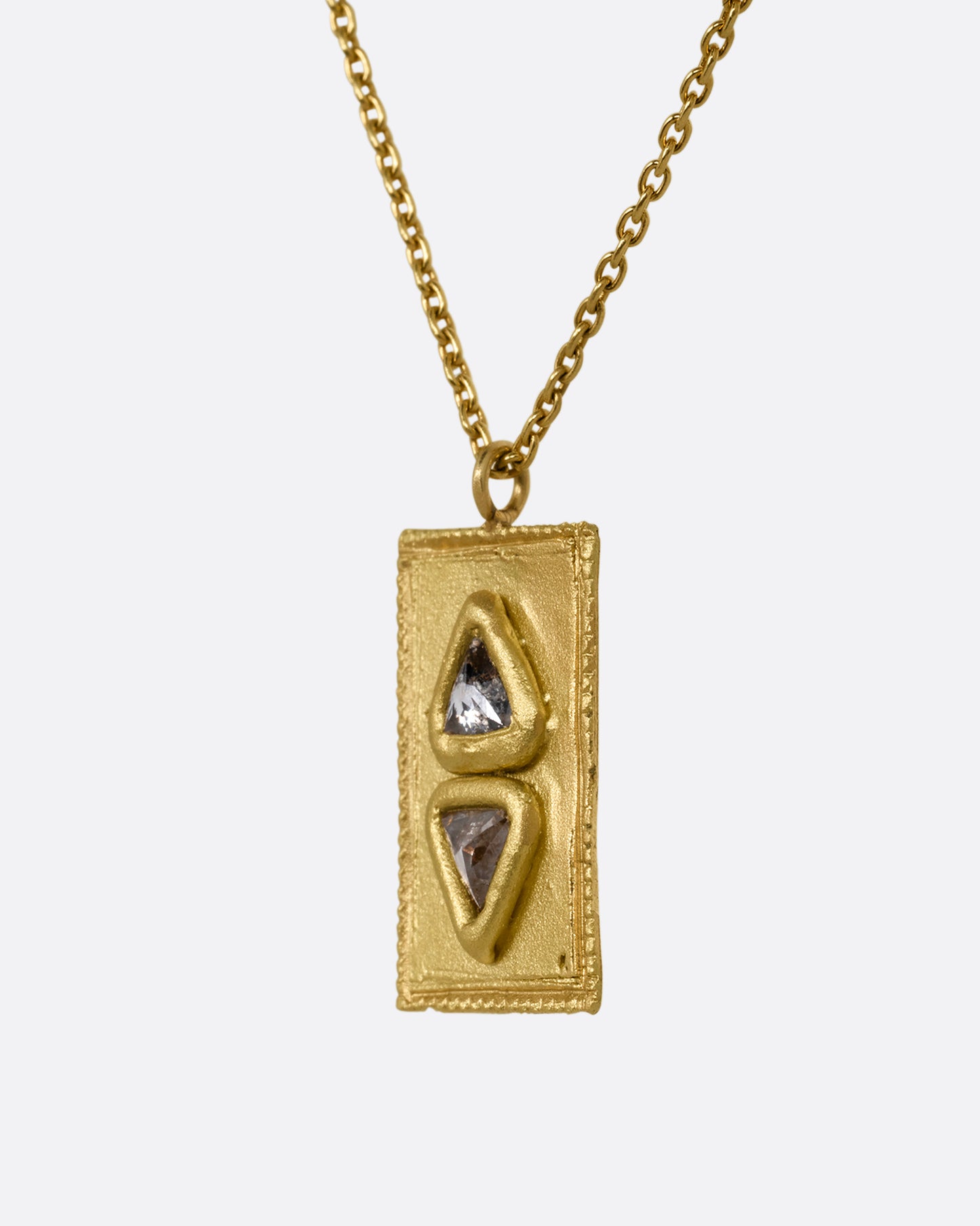 A cable chain necklace with two triangle shaped salt and pepper diamonds in a rectangle pendant. Shown from the side.