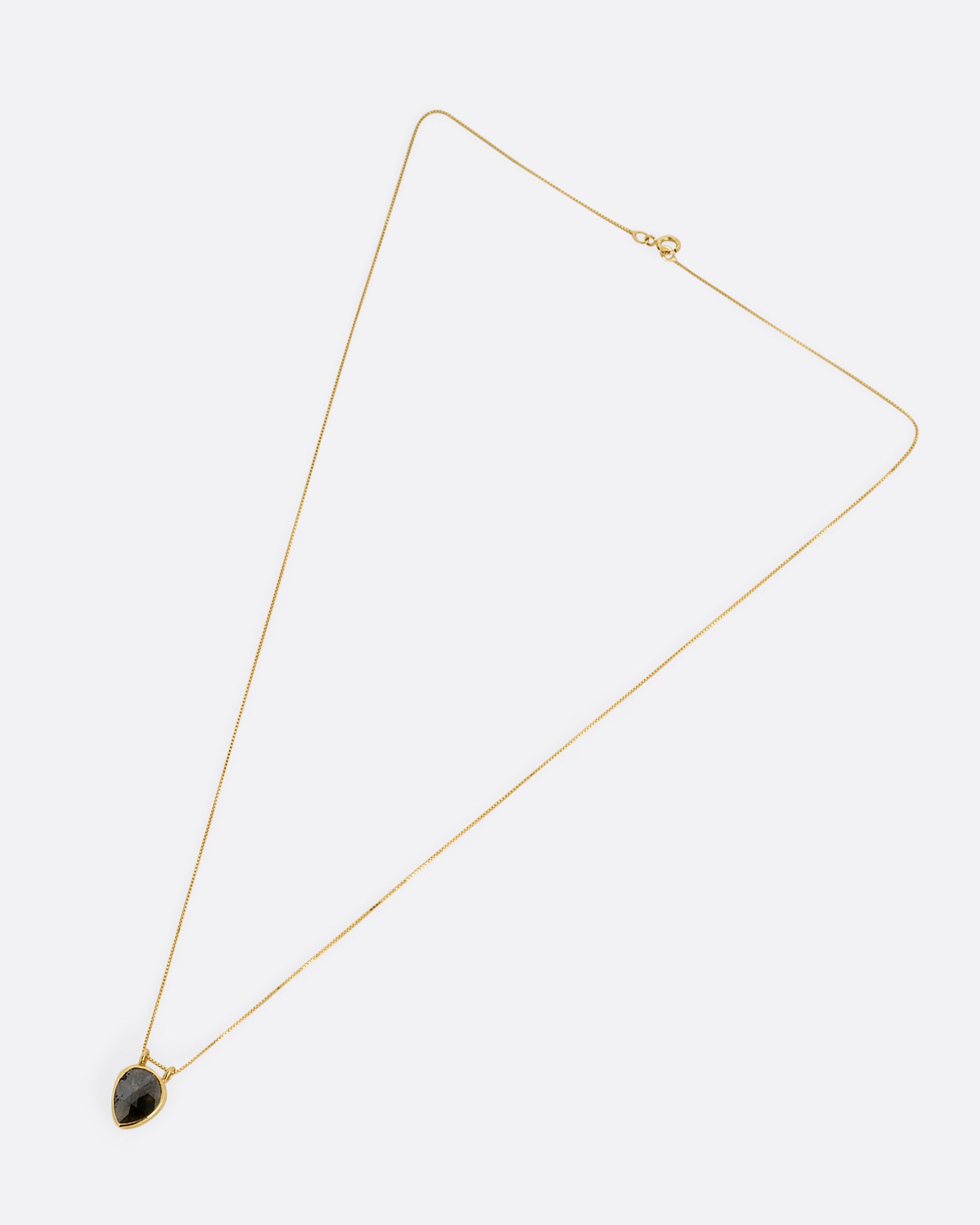 A yellow gold box chain necklace with a pear shaped salt and pepper diamond pendant shown from the front.