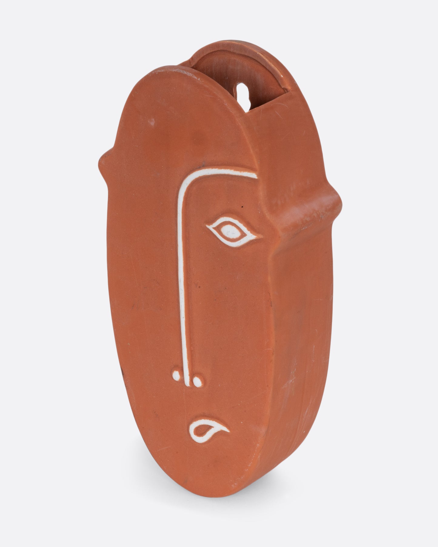 A terracotta face- shaped wall pocket with an opening at the top for plants. Shown from the side.