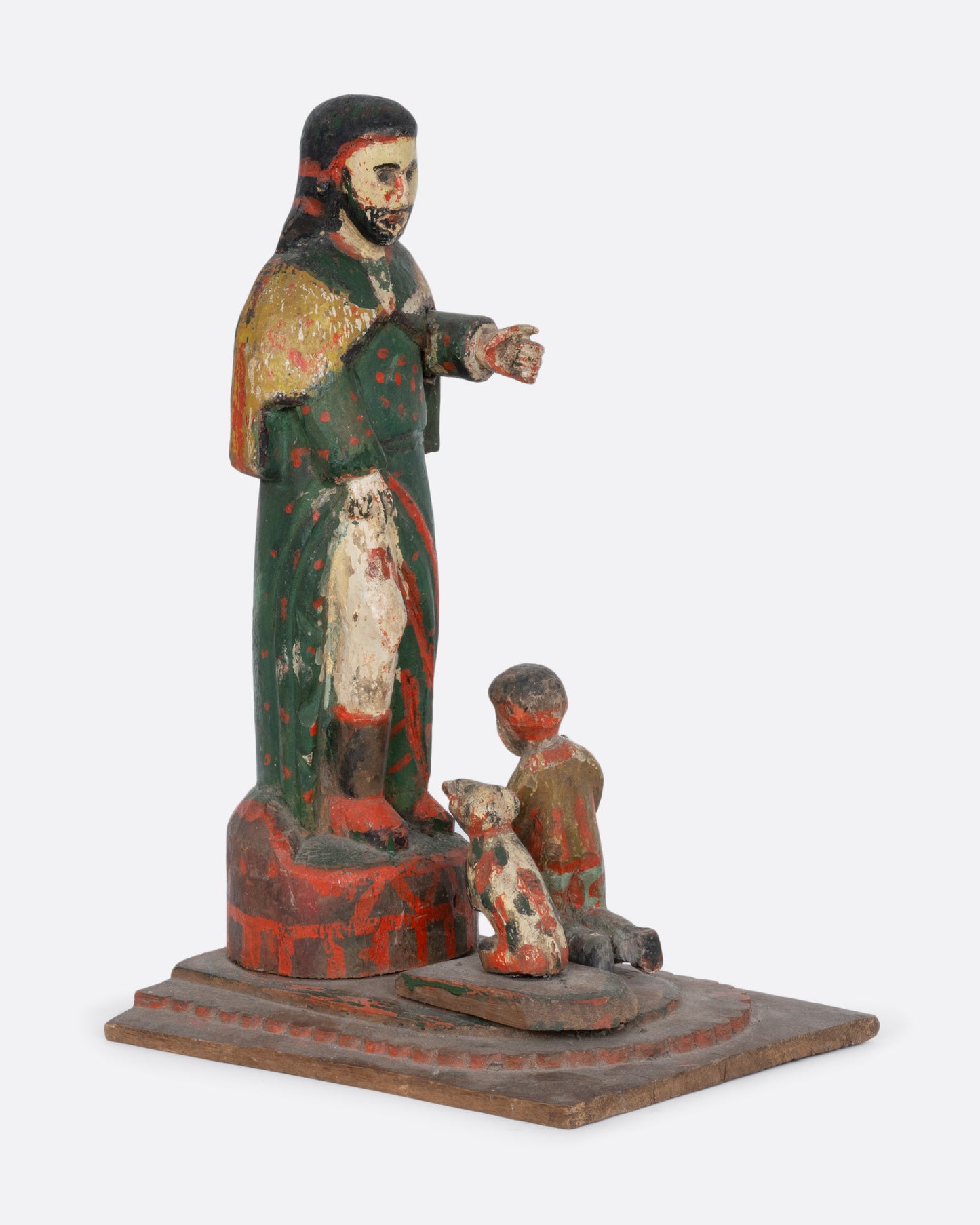 A wooden hand carved and painted Saint statue with a child and dog at its feet. Shown from the side.