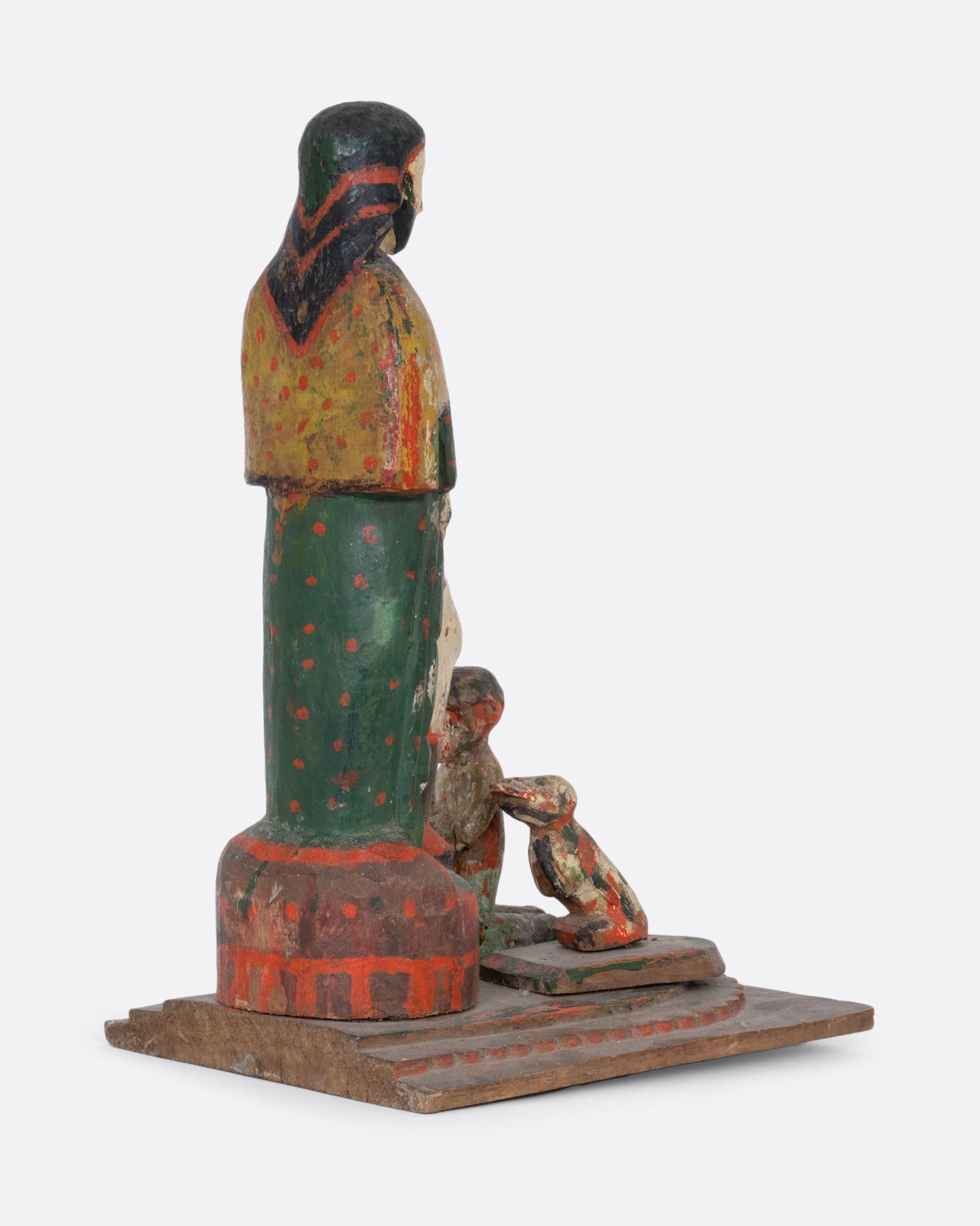 A wooden hand carved and painted Saint statue with a child and dog at its feet. Shown from the back.