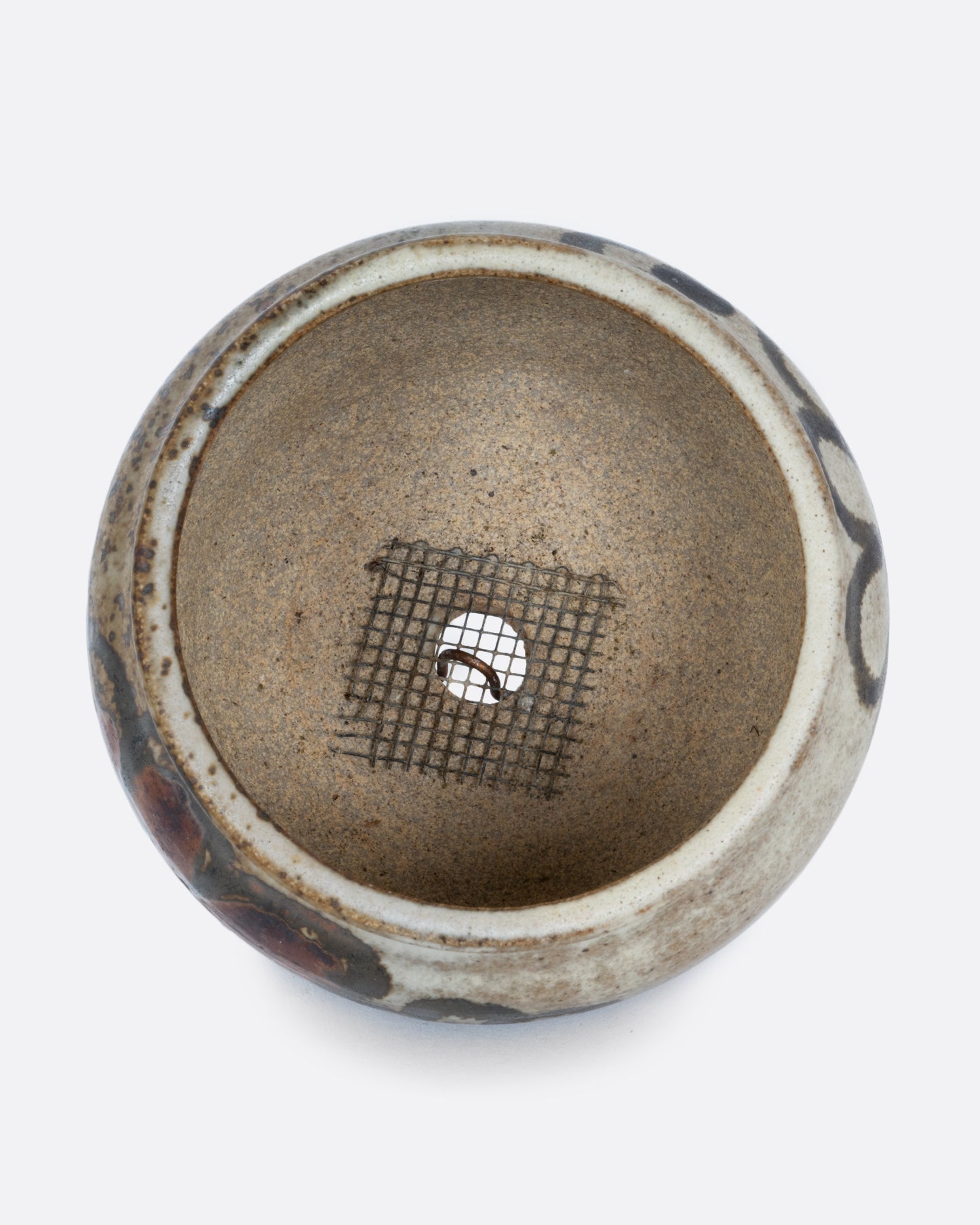 A pot with a brown handpainted pattern of flowers and a drainage hole at its base. Shown from the top.