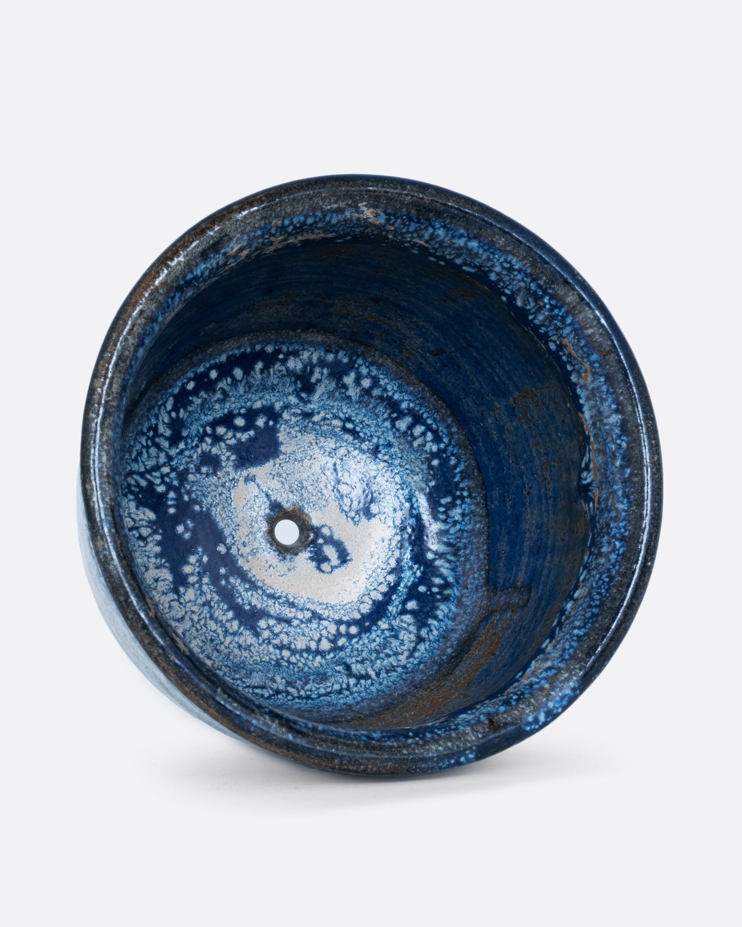 A pot with an azure glaze and drainage hole. Shown lying on its side from the top.