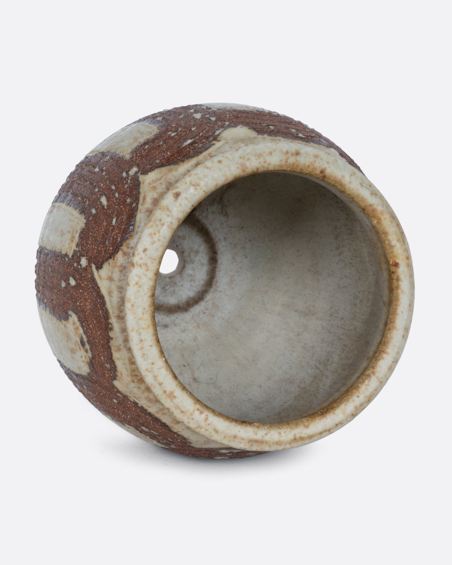A tan pot wreathed in russet- brown brush strokes with a drainage hole at its base. Shown on its side from the top.
