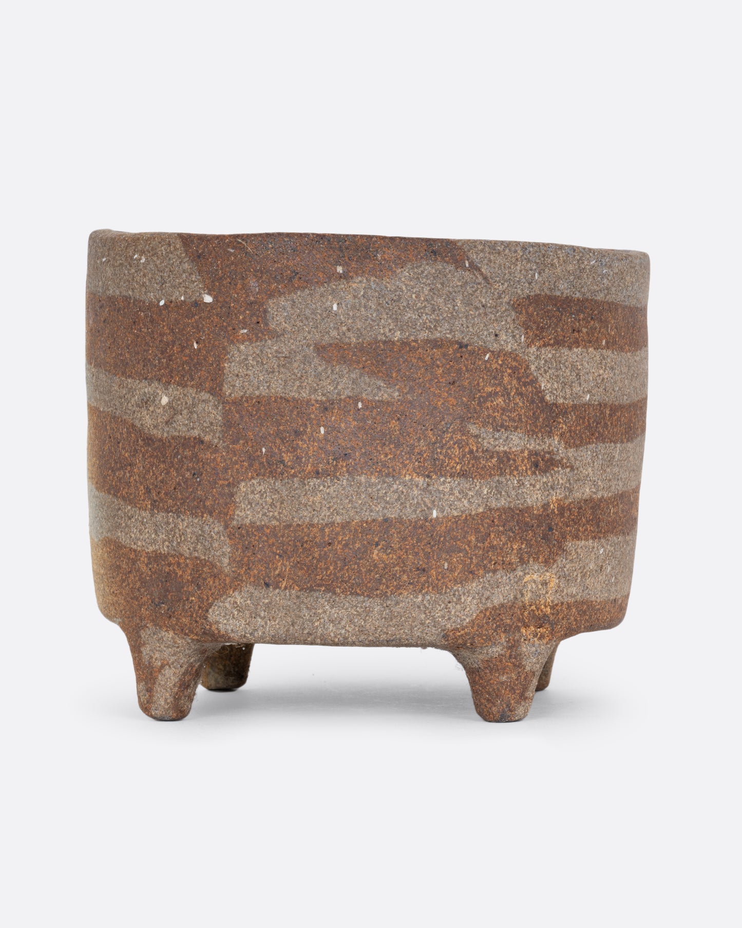 A brown ceramic footed pot with an all over geometric pattern and drainage hole. Shown from the side.
