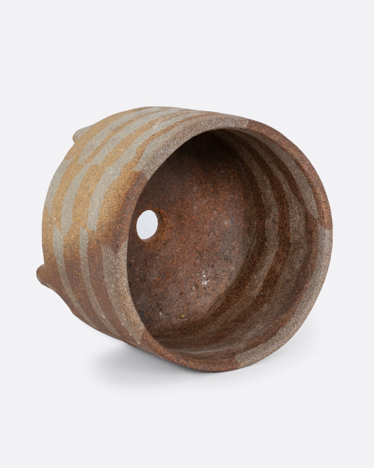 A brown ceramic footed pot with an all over geometric pattern and drainage hole. Shown lying on its side from the top.