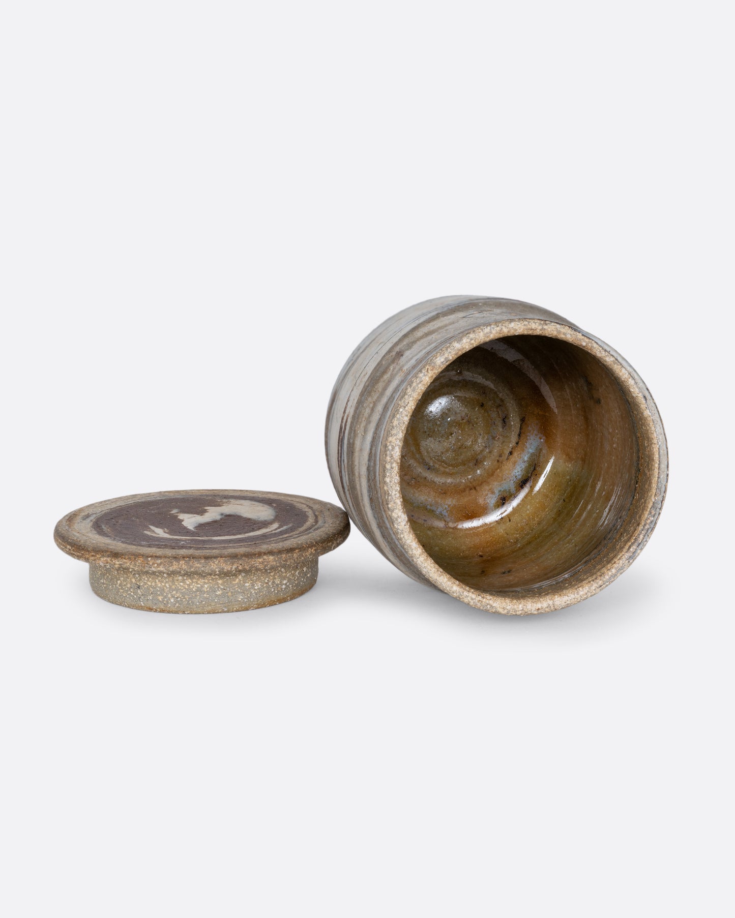 A lidded jar with a gray swirled matte exterior and glazed interior. Shown open lying on its side from the top with the lid at its side.