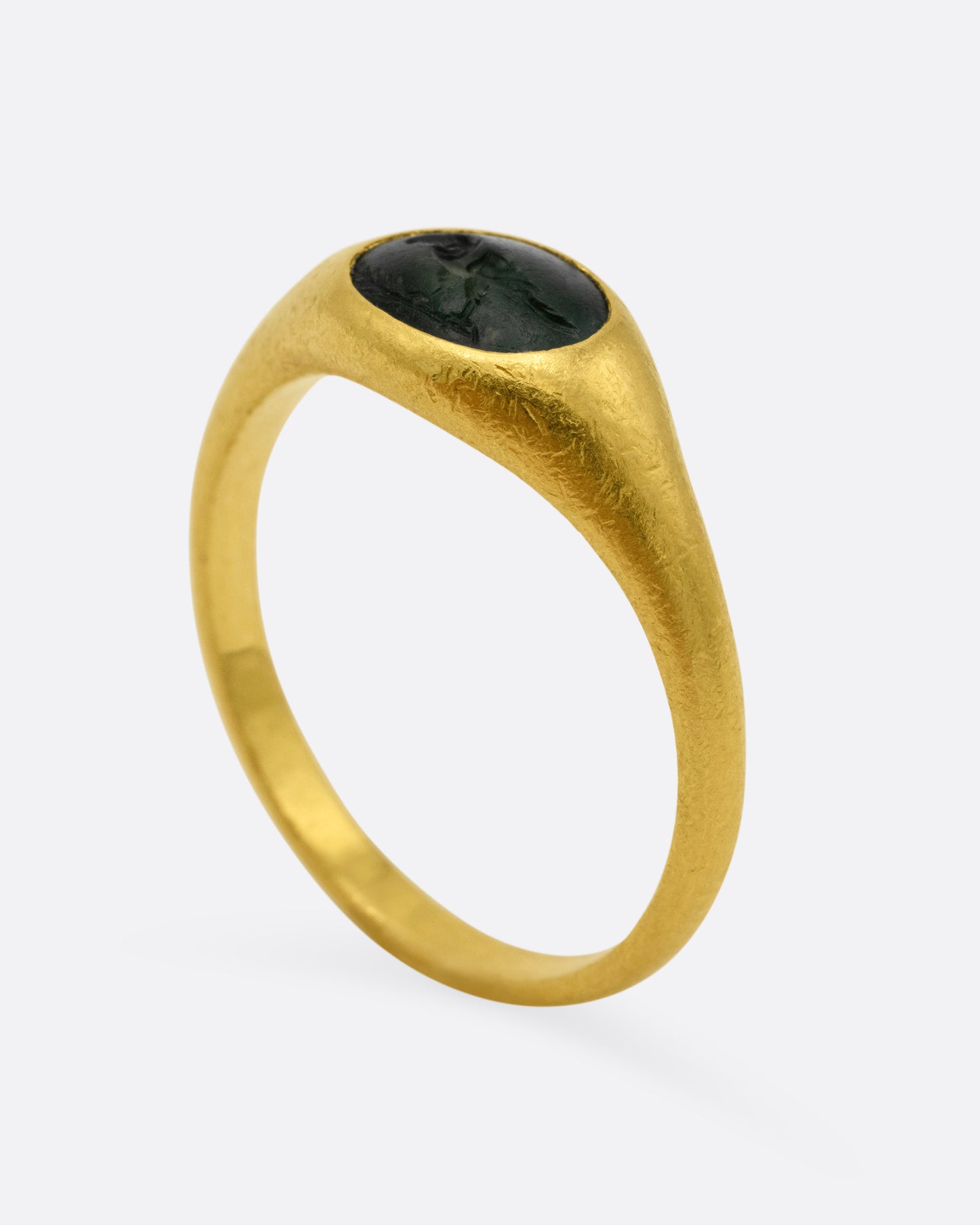 A yellow gold signet ring with a dark green chalcedony carved with a parrot, shown from the side standing up.