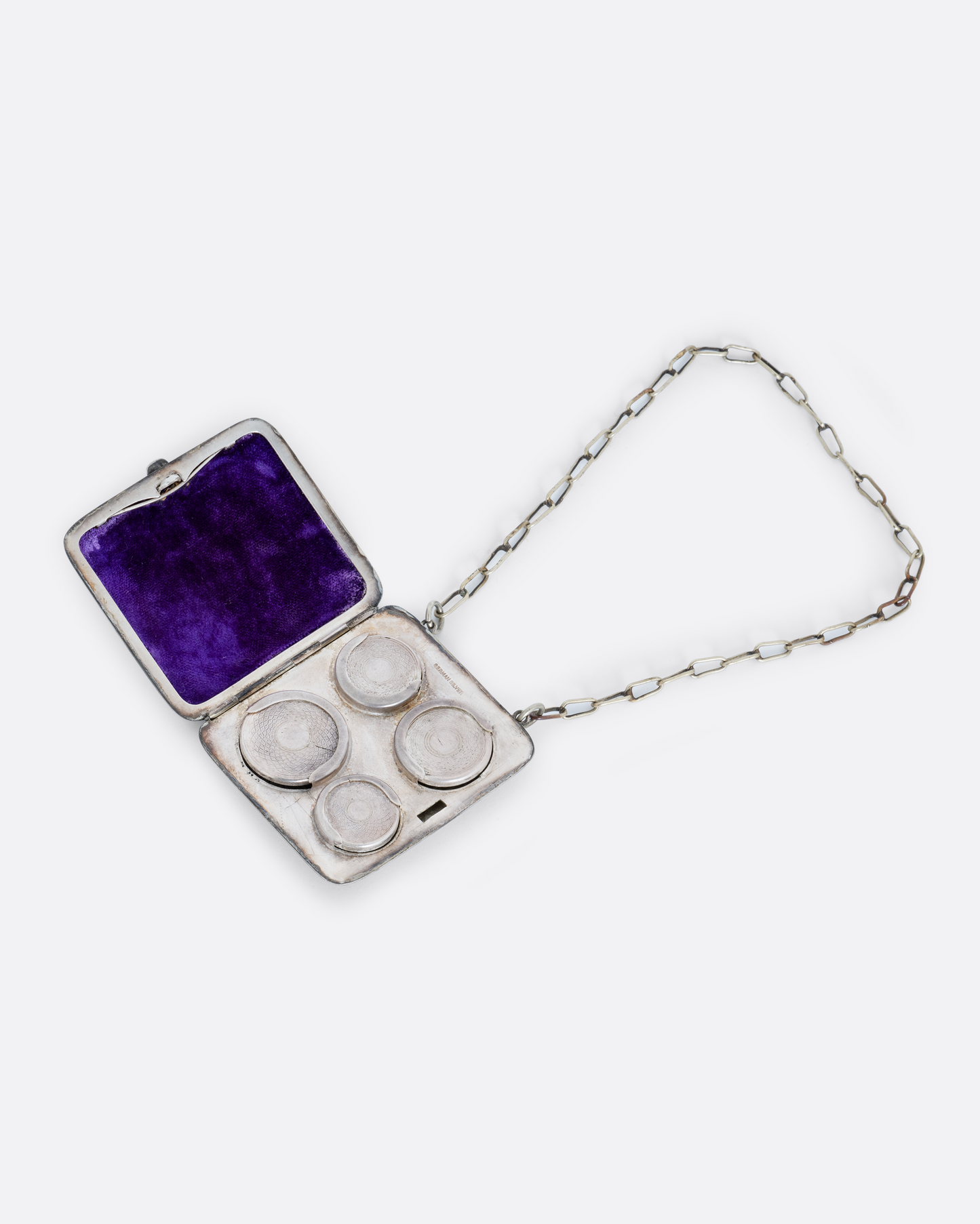 A silver square velvet lined coin purse with a cable wrist chain. Shown open lying flat.