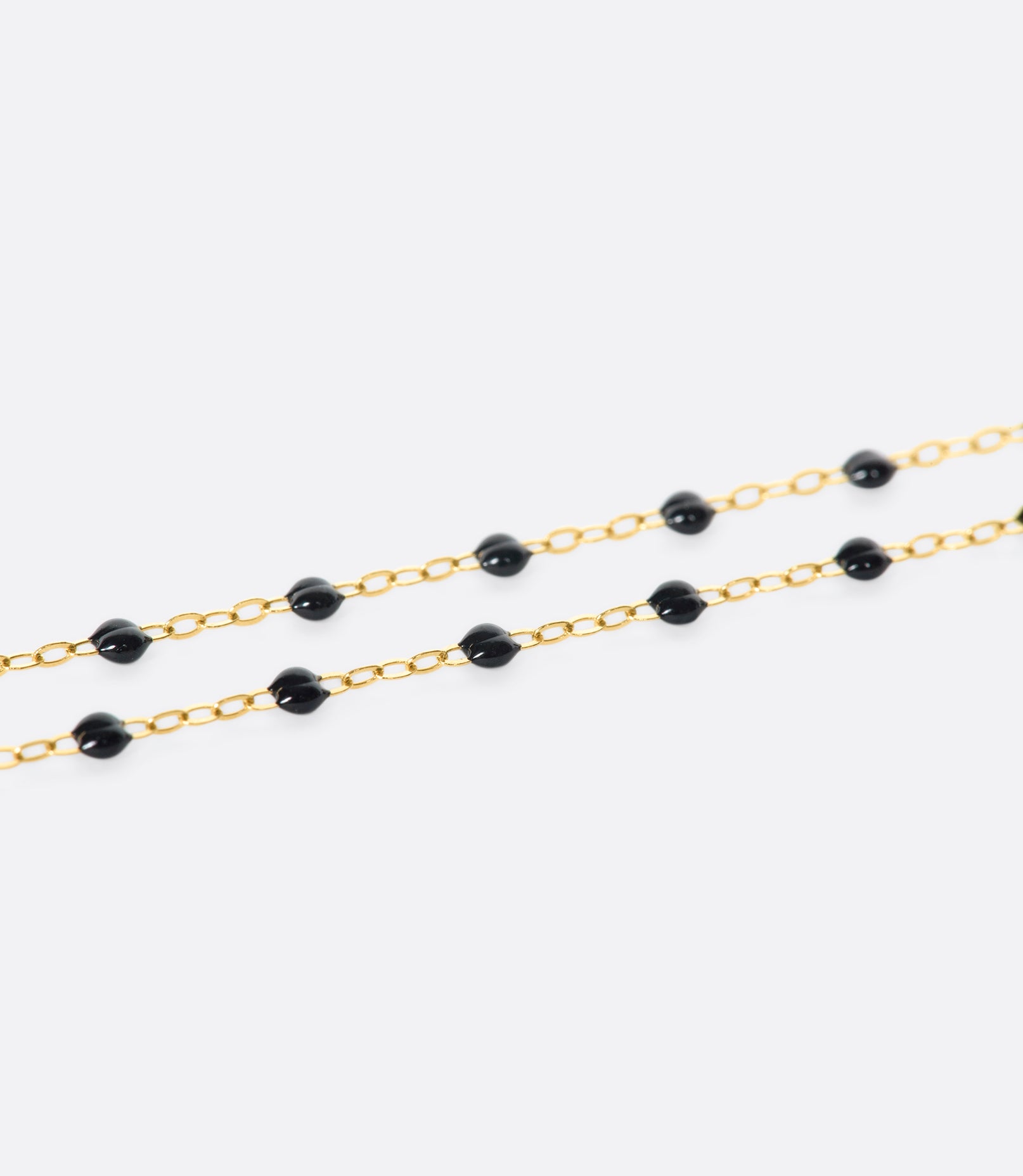 A close up view of a yellow gold cable chain bracelet with black resin droplets.