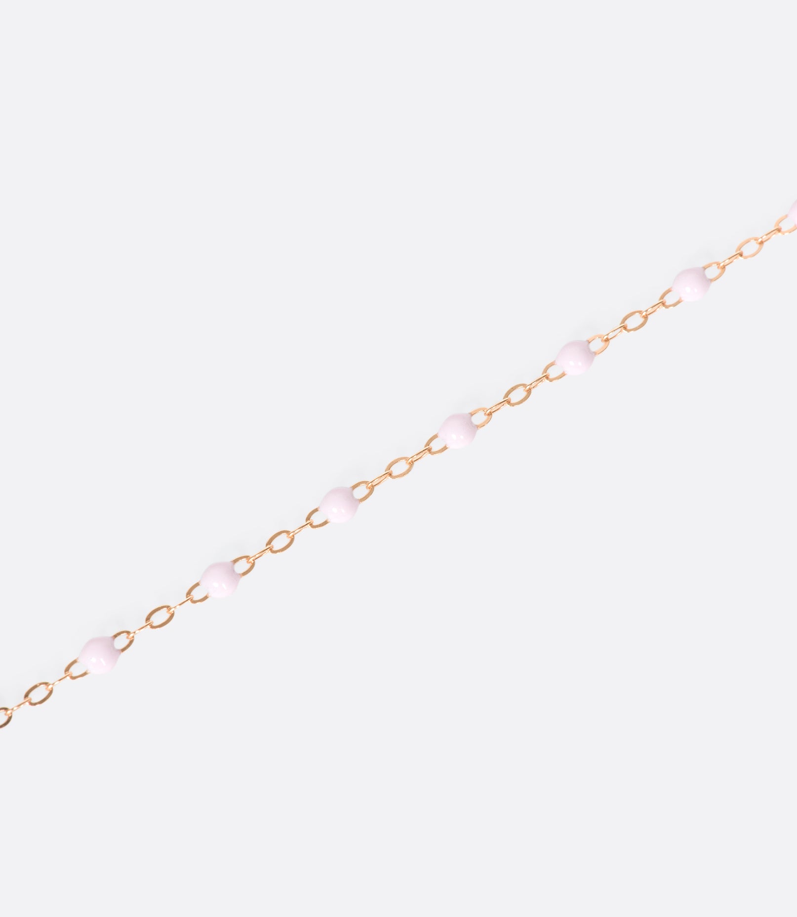 A close up view of a yellow gold cable chain bracelet with pink resin droplets.