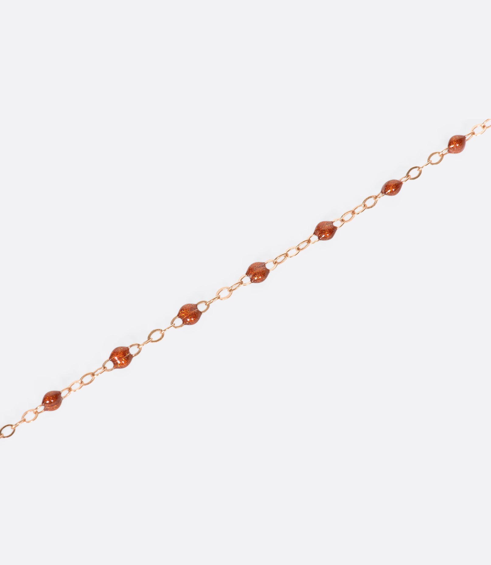 A close up view of a yellow gold cable chain bracelet with rusty red resin droplets.