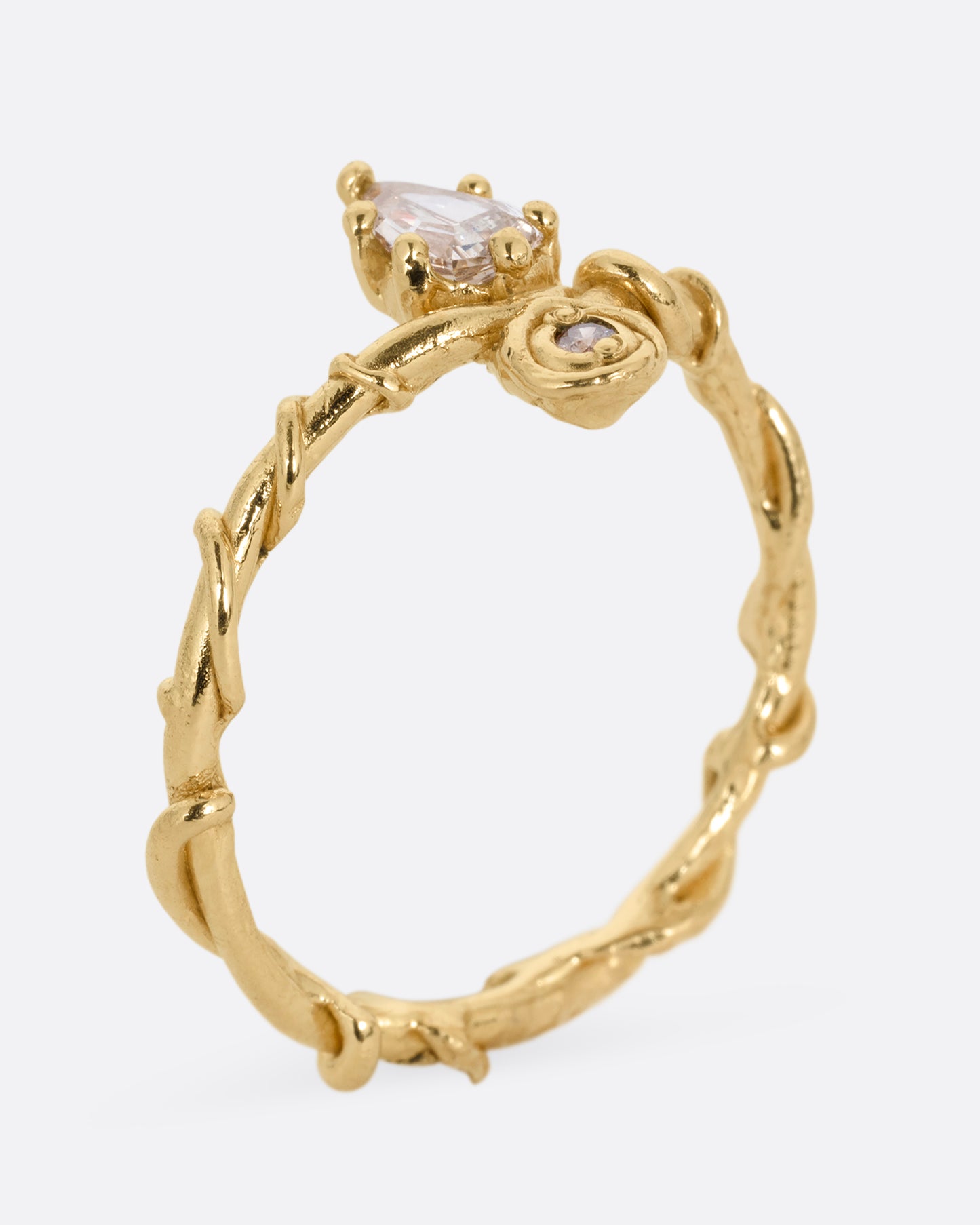 A yellow gold ring with a vine wrapped band and two stacked diamonds, one pear one round. Shown from the side, standing up.