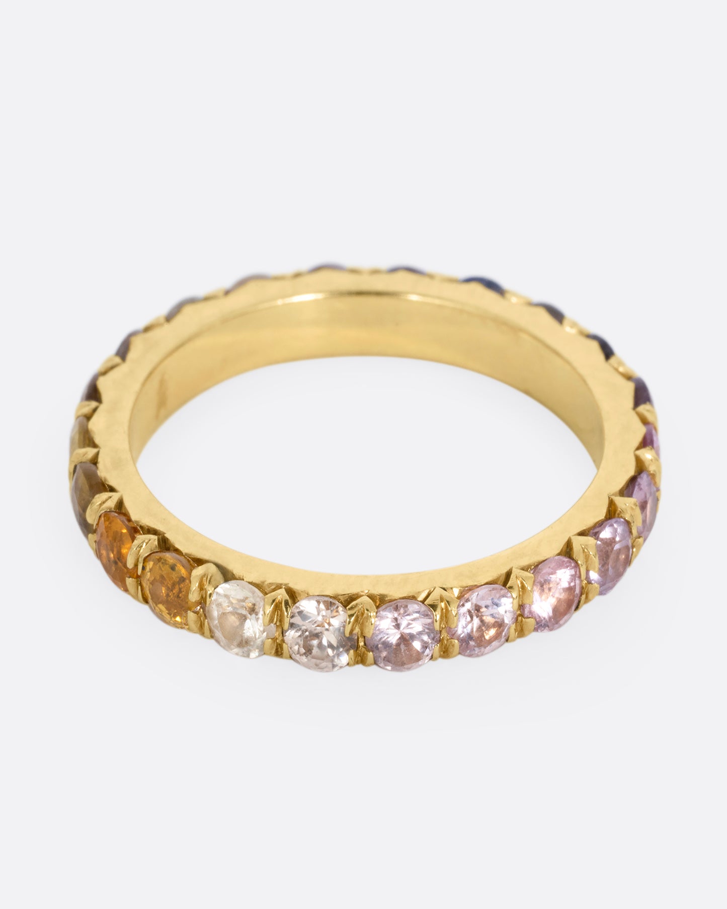 A yellow gold eternity band with multicolored sapphires. Shown from the front.