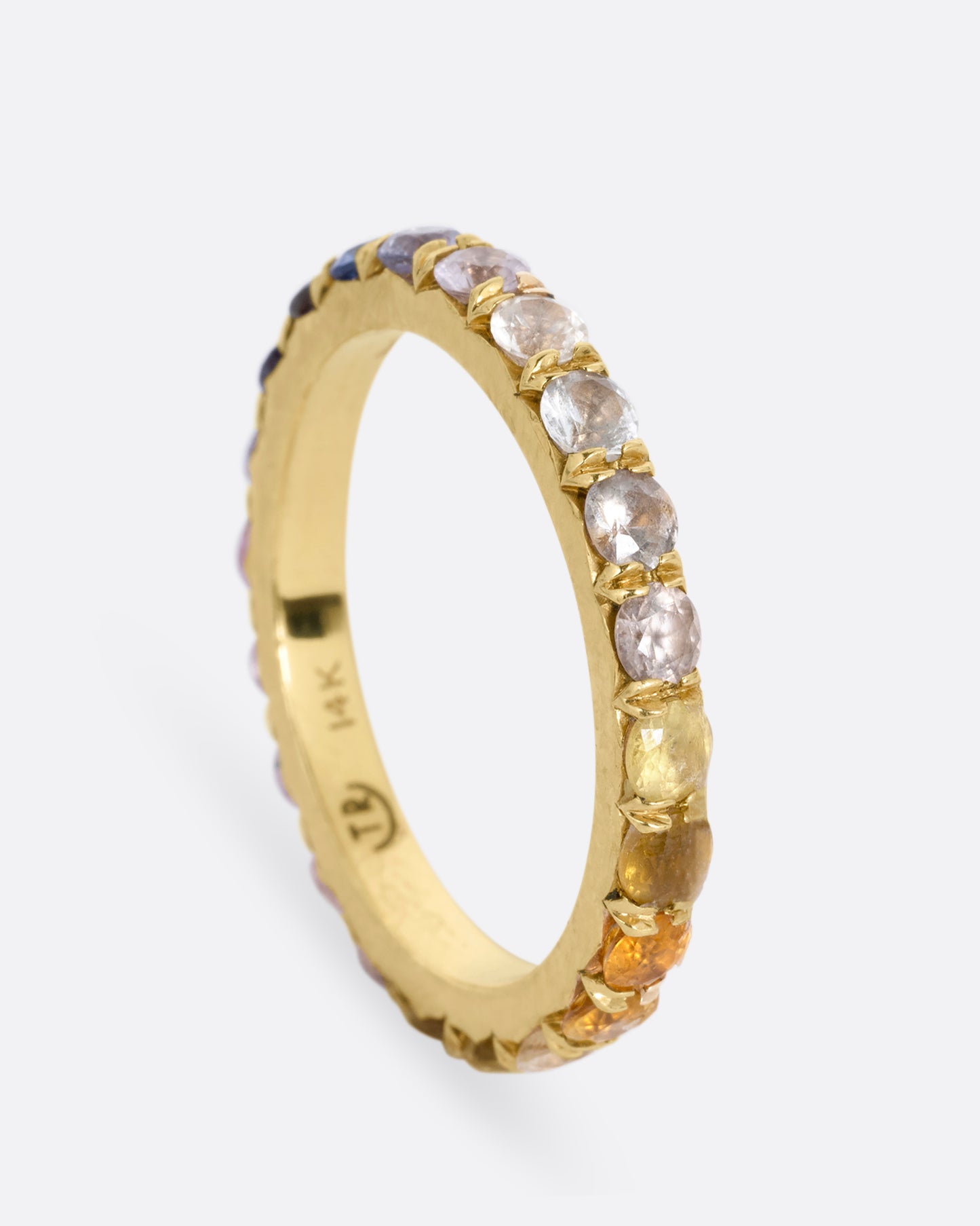 A yellow gold eternity band with multicolored sapphires. Shown from the side standing up.