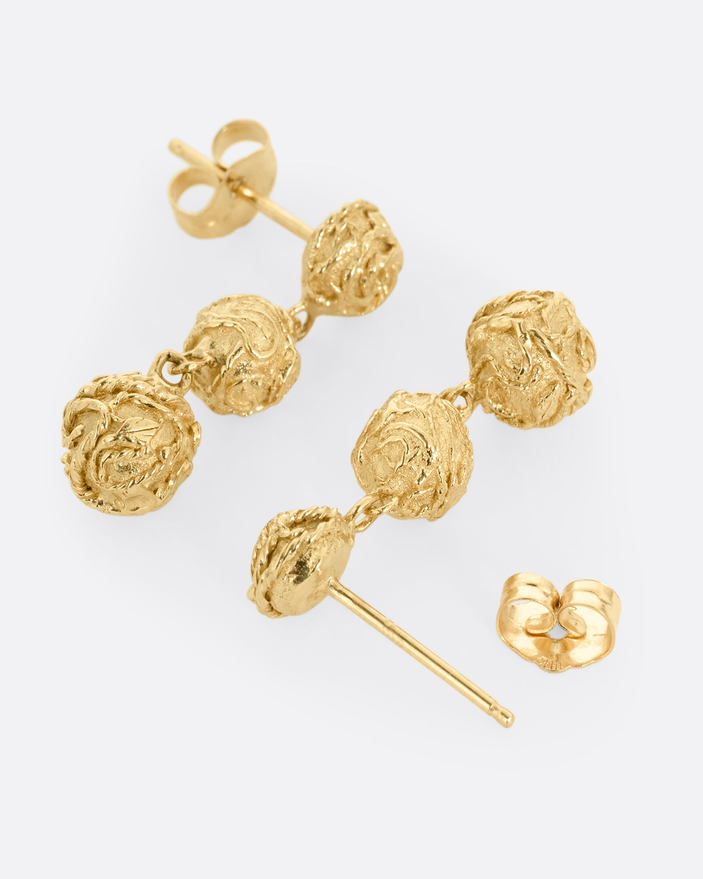A pair of yellow gold dangle earrings with three linked spheres. Shown lying flat from the side. One earring its facing front, the other is open facing back.