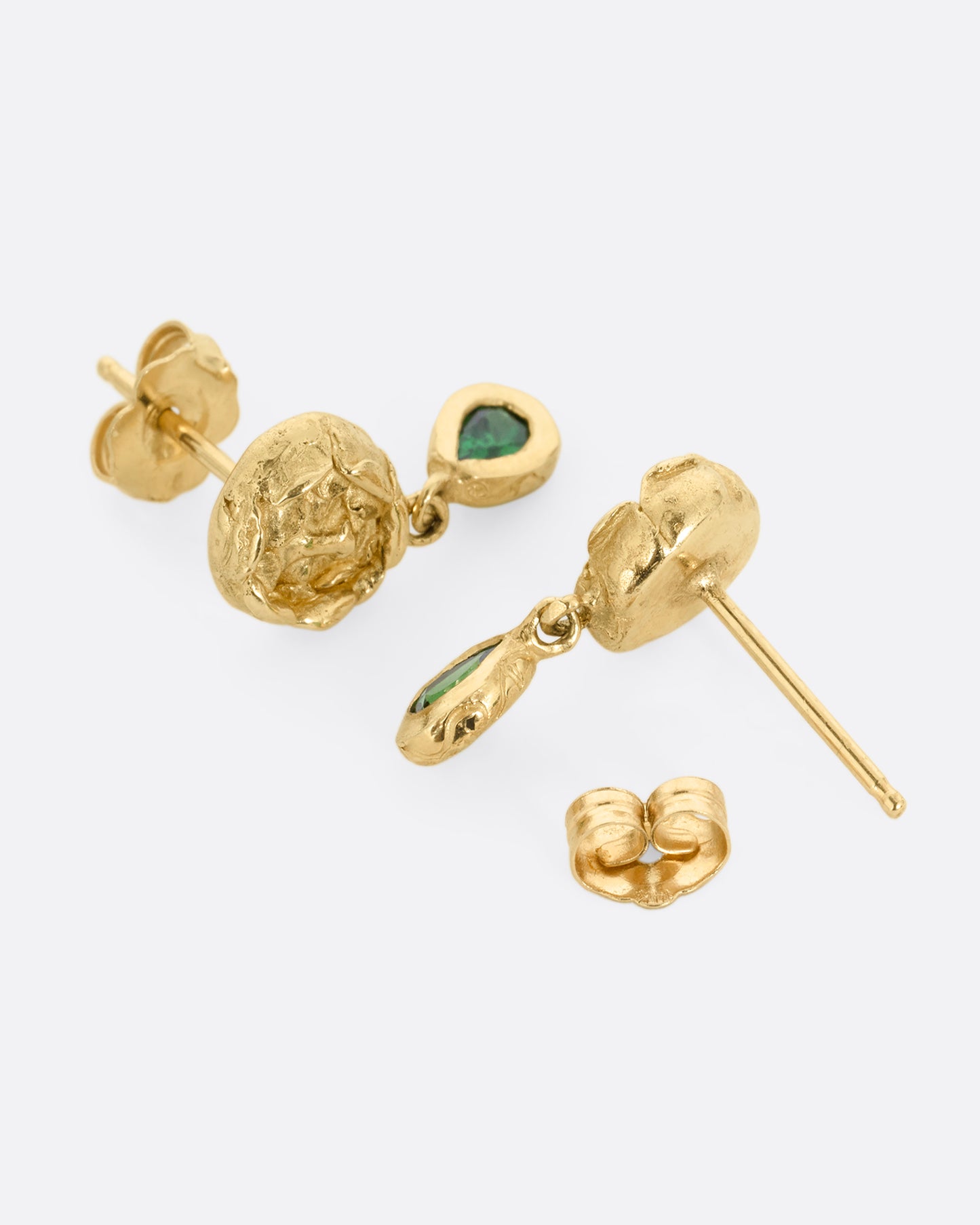 A pair of yellow gold studback earrings with faces at the center of rosebuds and a pear shaped tsavorite dangle. Shown laying down, with the back removed.
