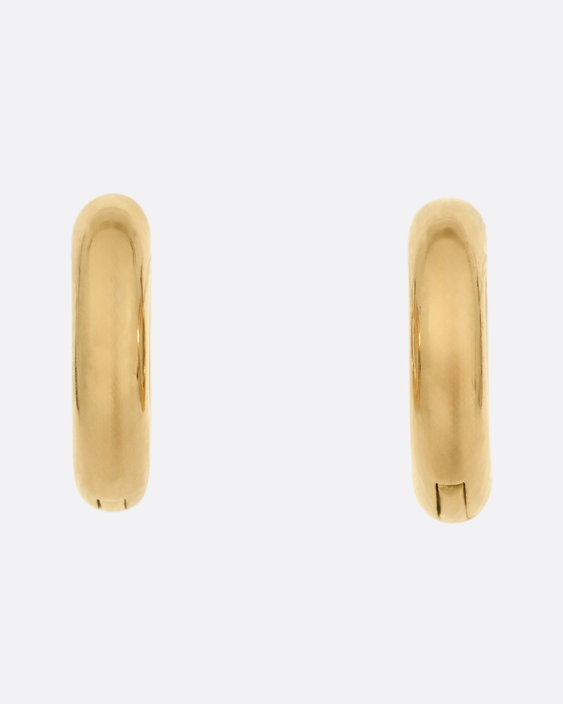 A pair of yellow gold huggie hoops with hinges and clicker clasps, shown from the front.