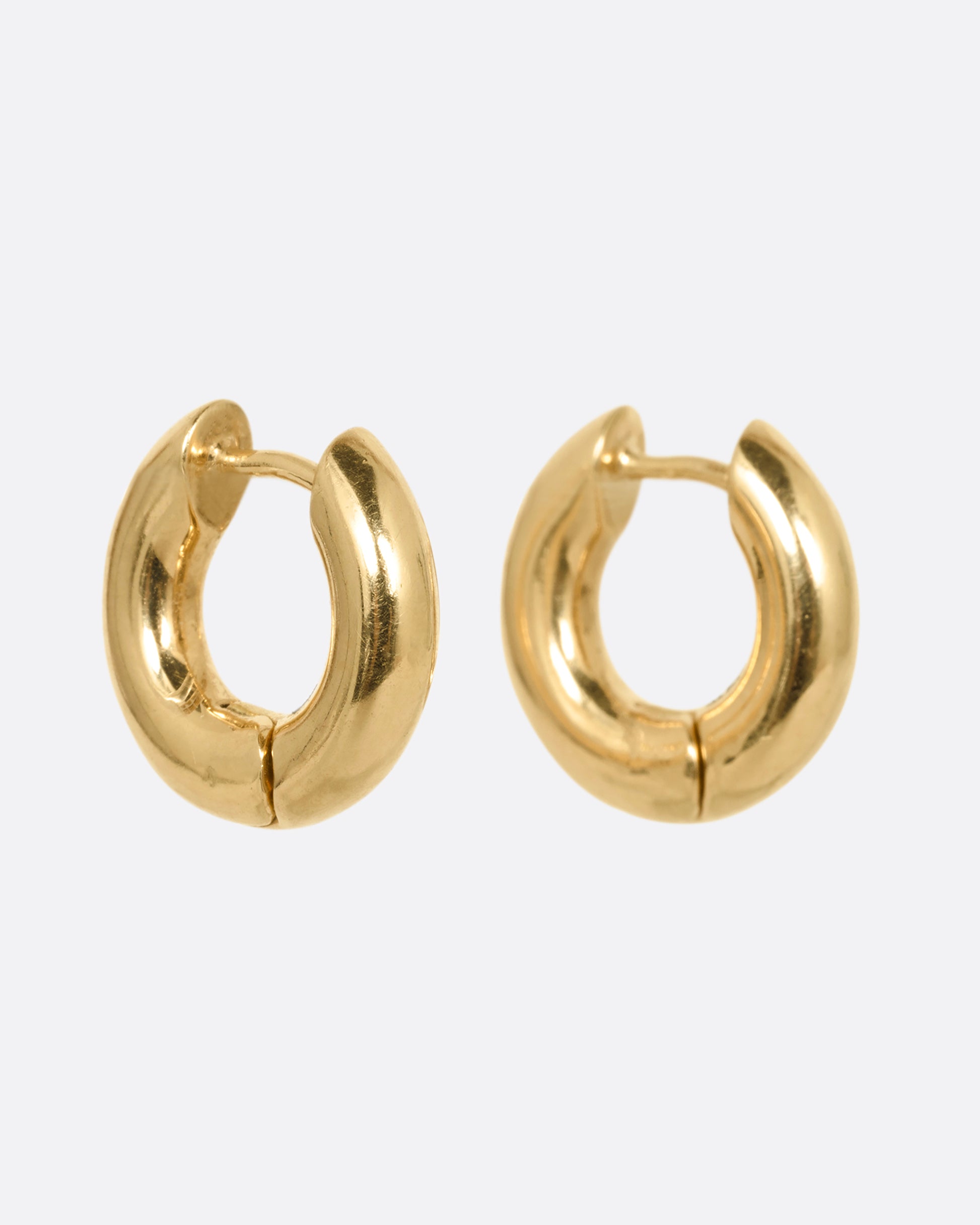 A pair of yellow gold huggie hoops with hinges and clicker clasps, shown from the side.