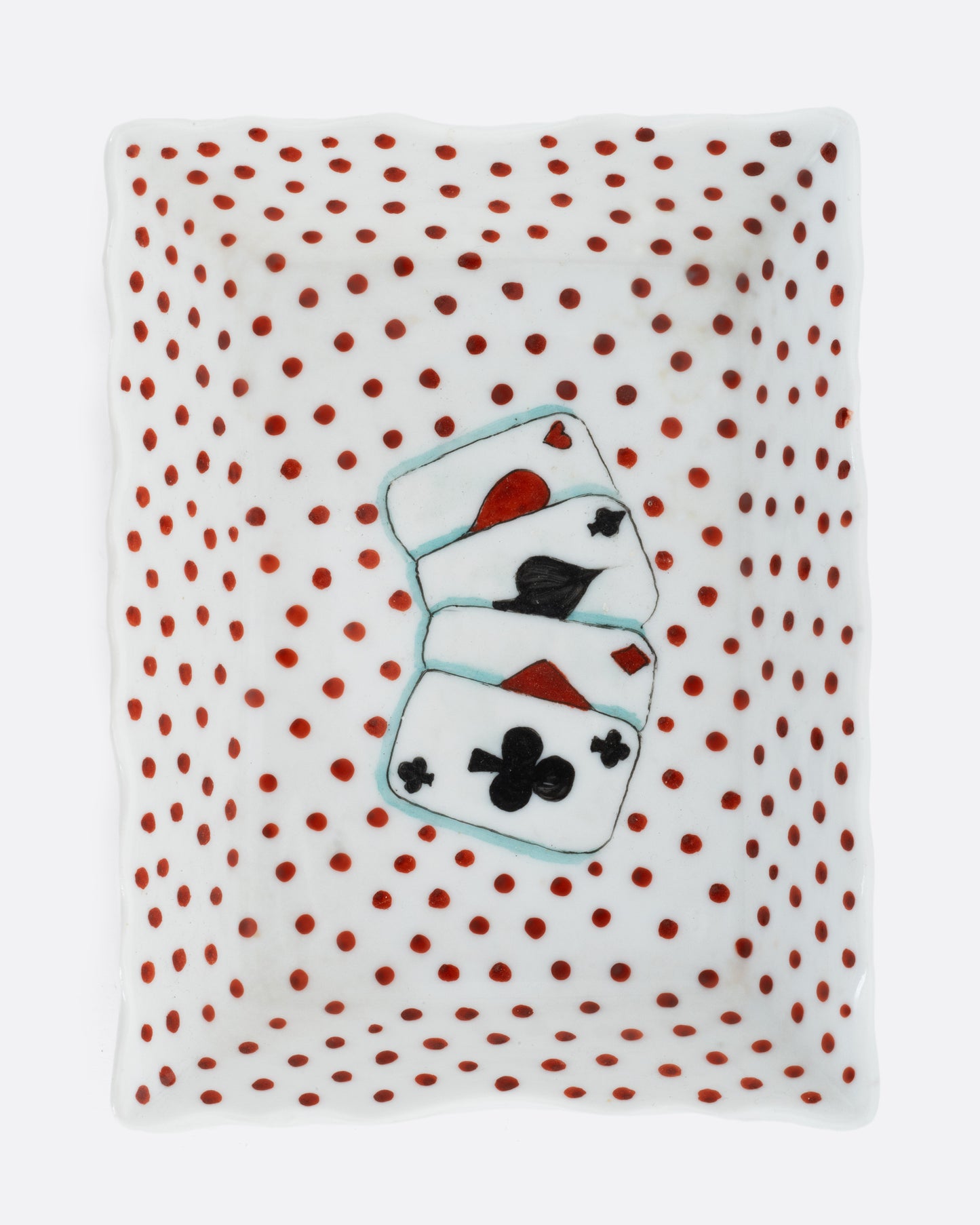 A white rectangular ceramic dish with red hand painted polkadots, and four playing cards at the center. Shown from the top.