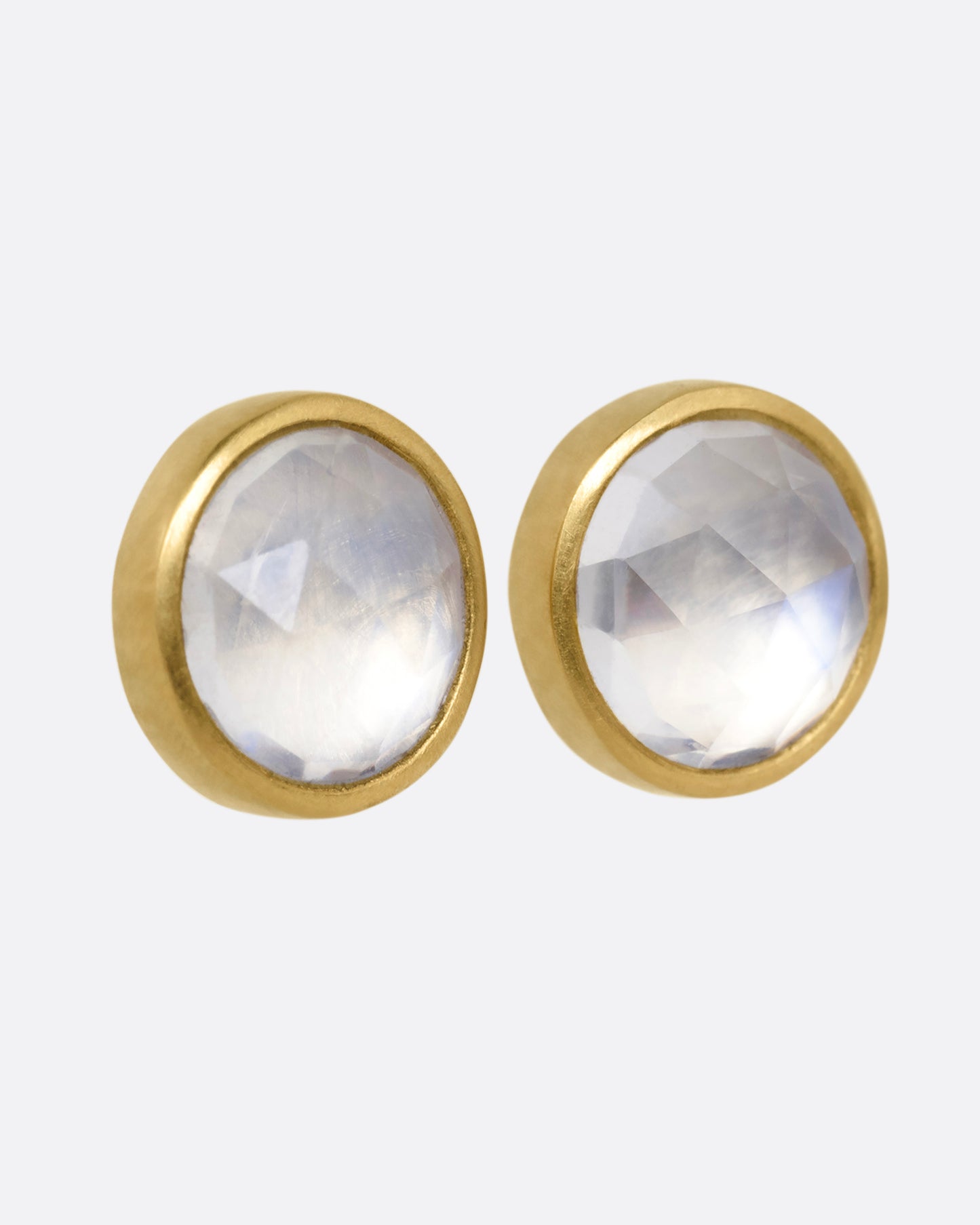 A pair of yellow gold stud earrings with moonstones. Shown from the side.