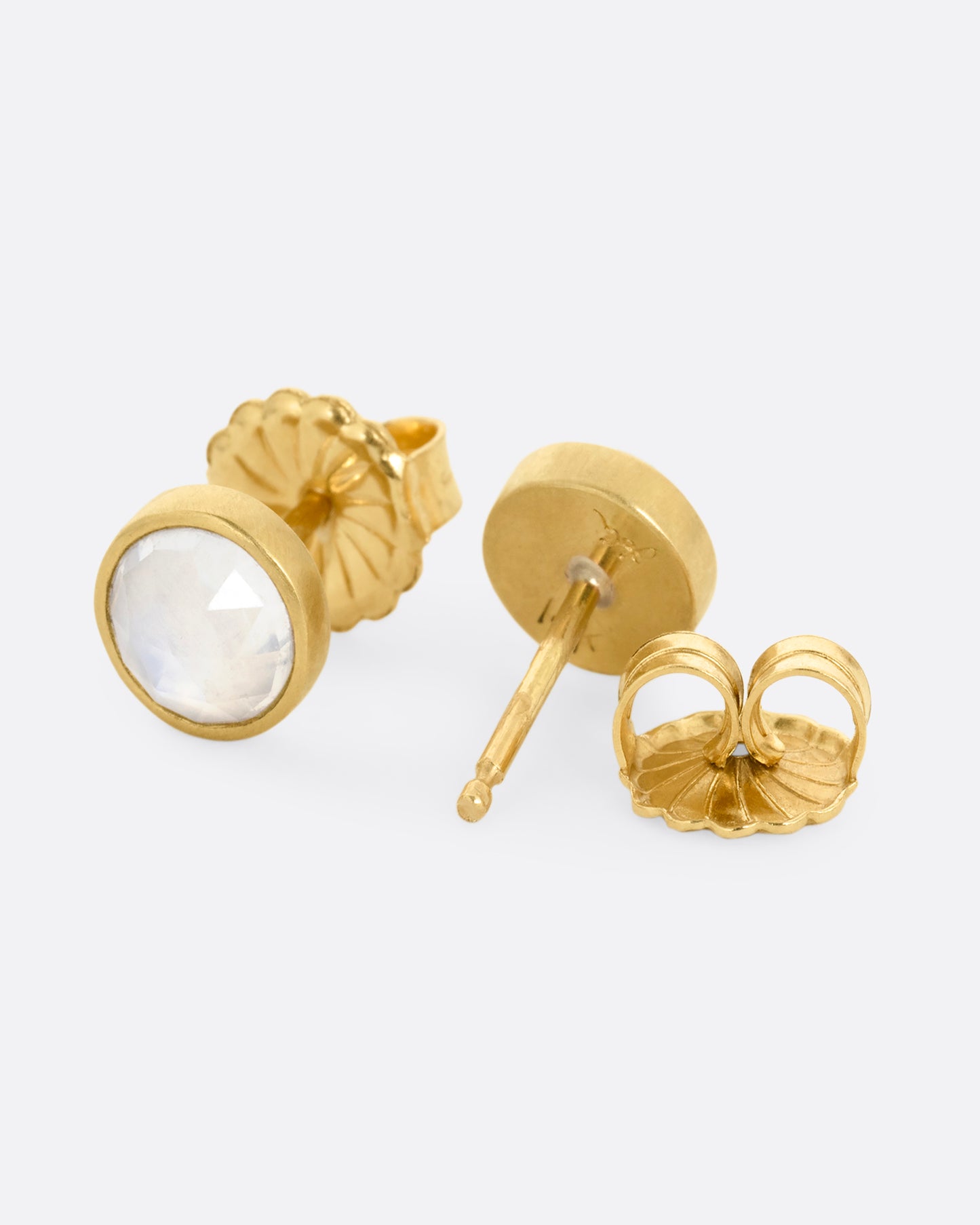 A pair of yellow gold stud earrings with moonstones. One earring is shown from the front, the other is open from the back.