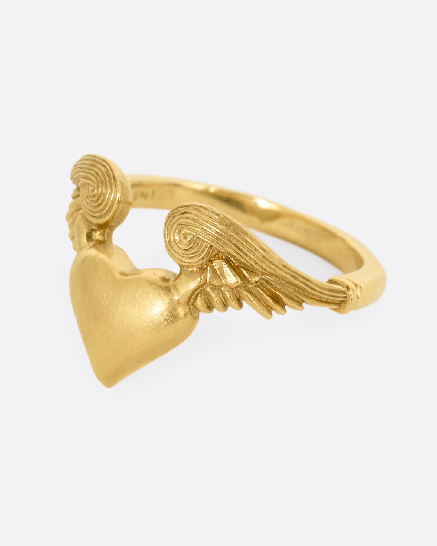A yellow gold ring with a heart with wings on it. Shown from the side.