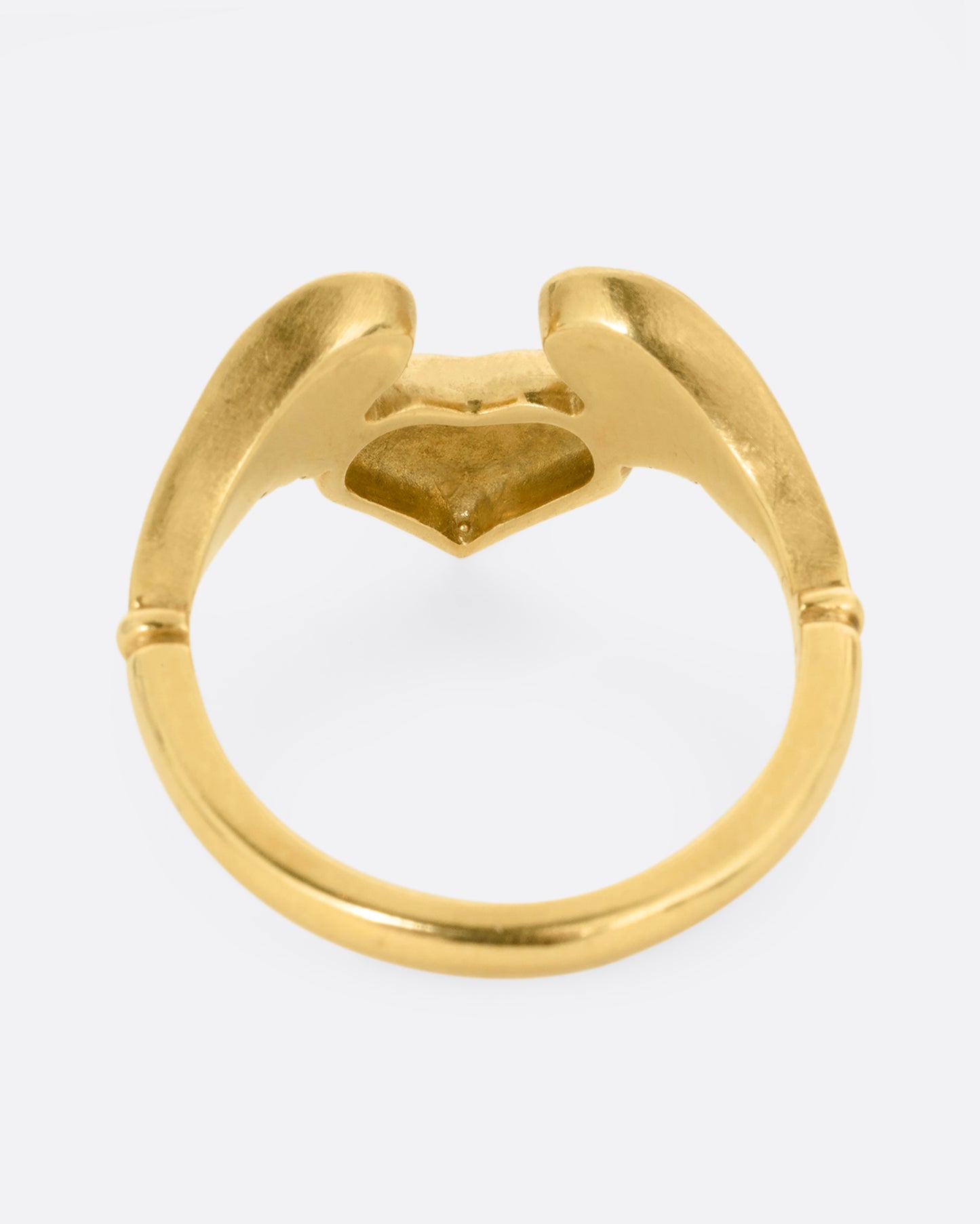 A yellow gold ring with a heart with wings on it. Shown from the back.