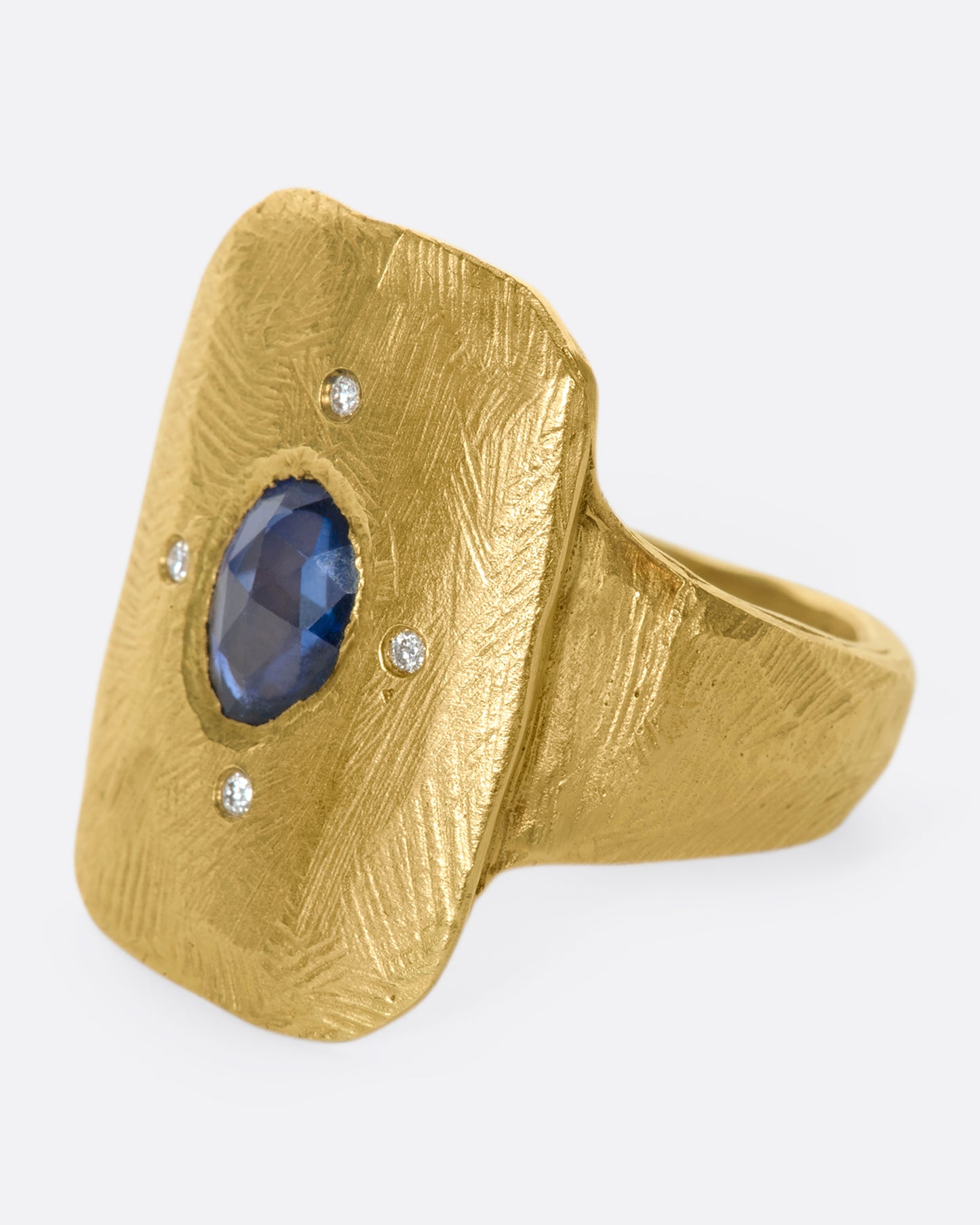 An 18k gold hand carved cocktail ring with a rose-cut, dark blue sapphire dotted with four star-like diamonds