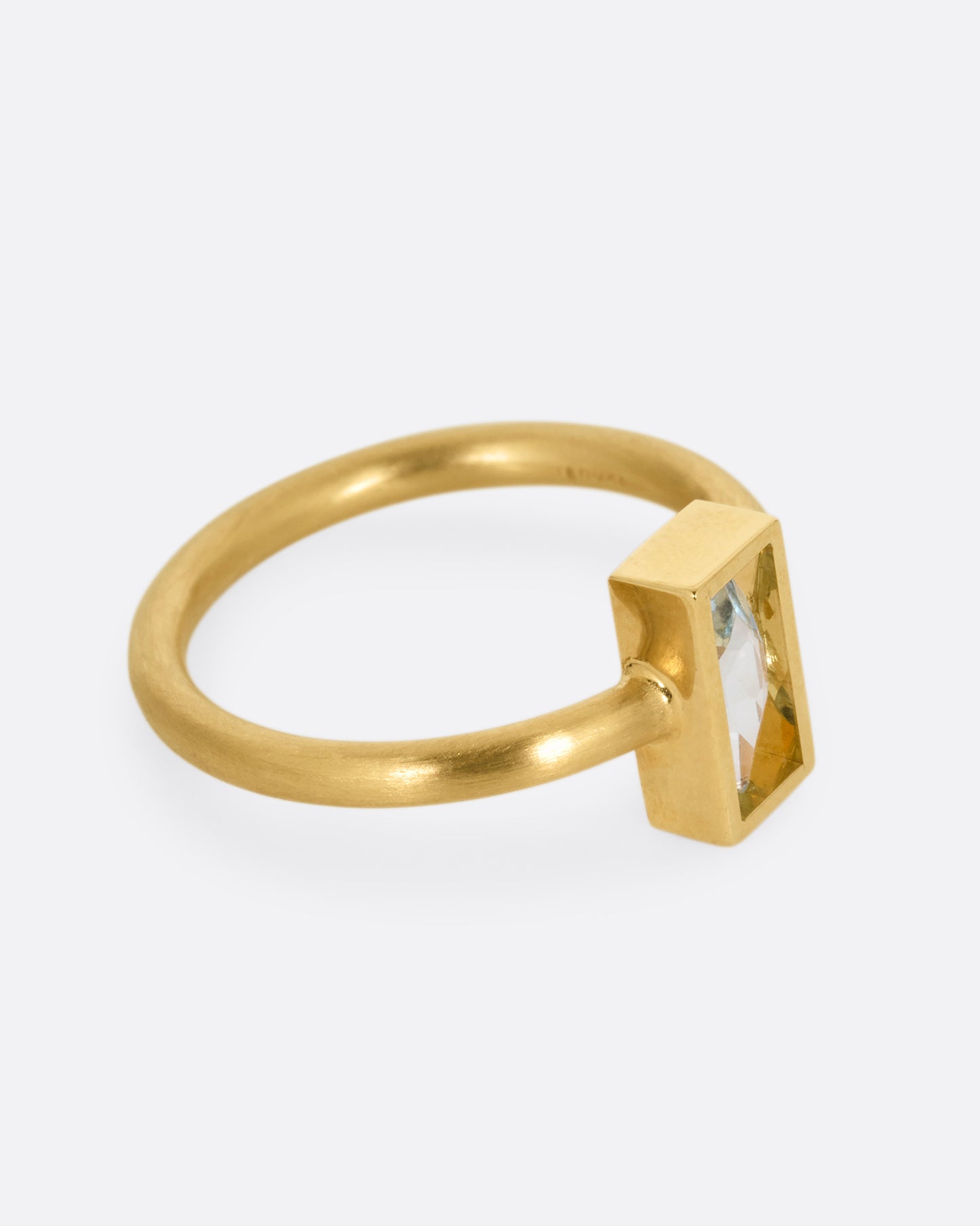 A yellow gold ring with an aquamarine in an open rectangular setting. Shown from the side.