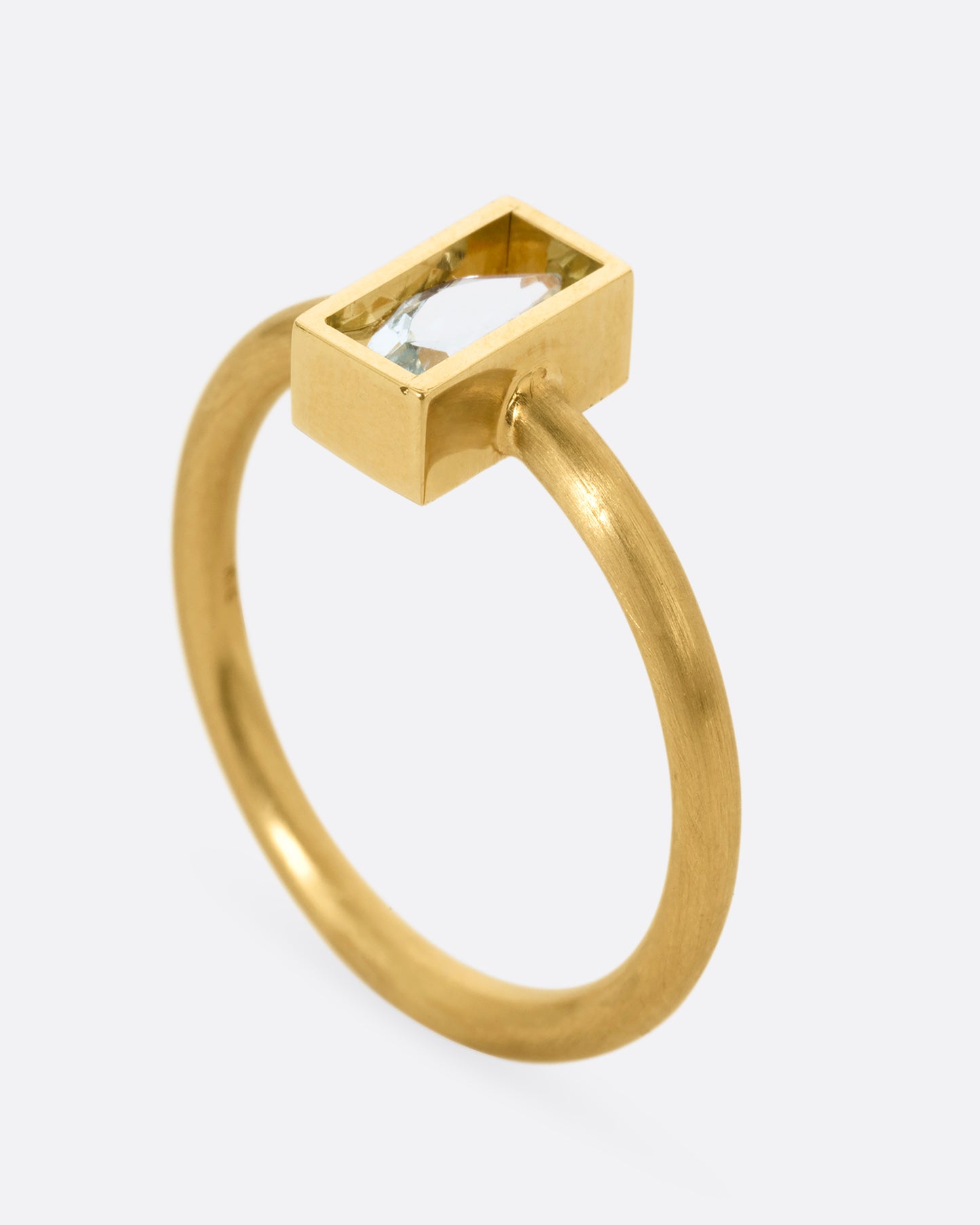 A yellow gold ring with an aquamarine in an open rectangular setting. Shown standing up from the side.