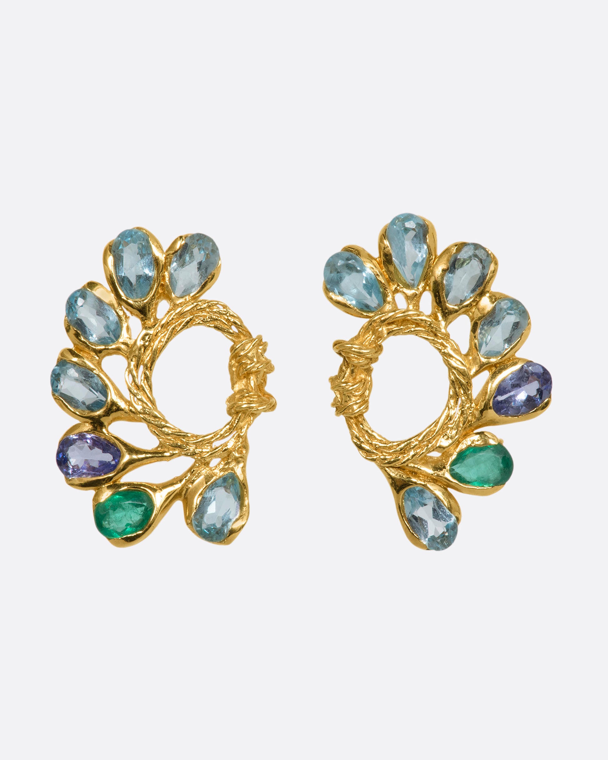 A pair of yellow gold circular twisted stud earrings feathered with oval emeralds, tanzanites, and topaz. View from the front.
