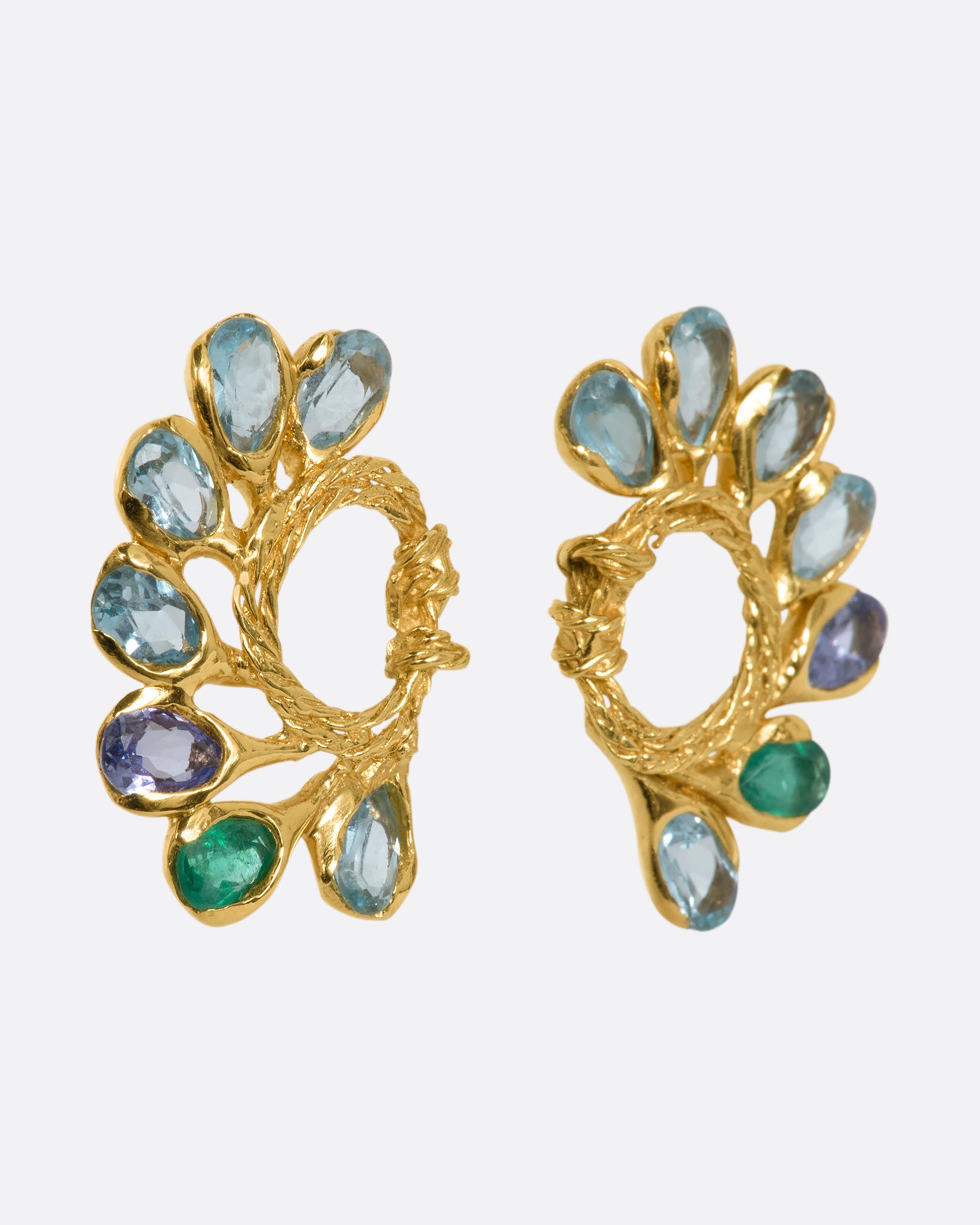 A pair of yellow gold circular twisted stud earrings feathered with oval emeralds, tanzanites, and topaz. View from the side.