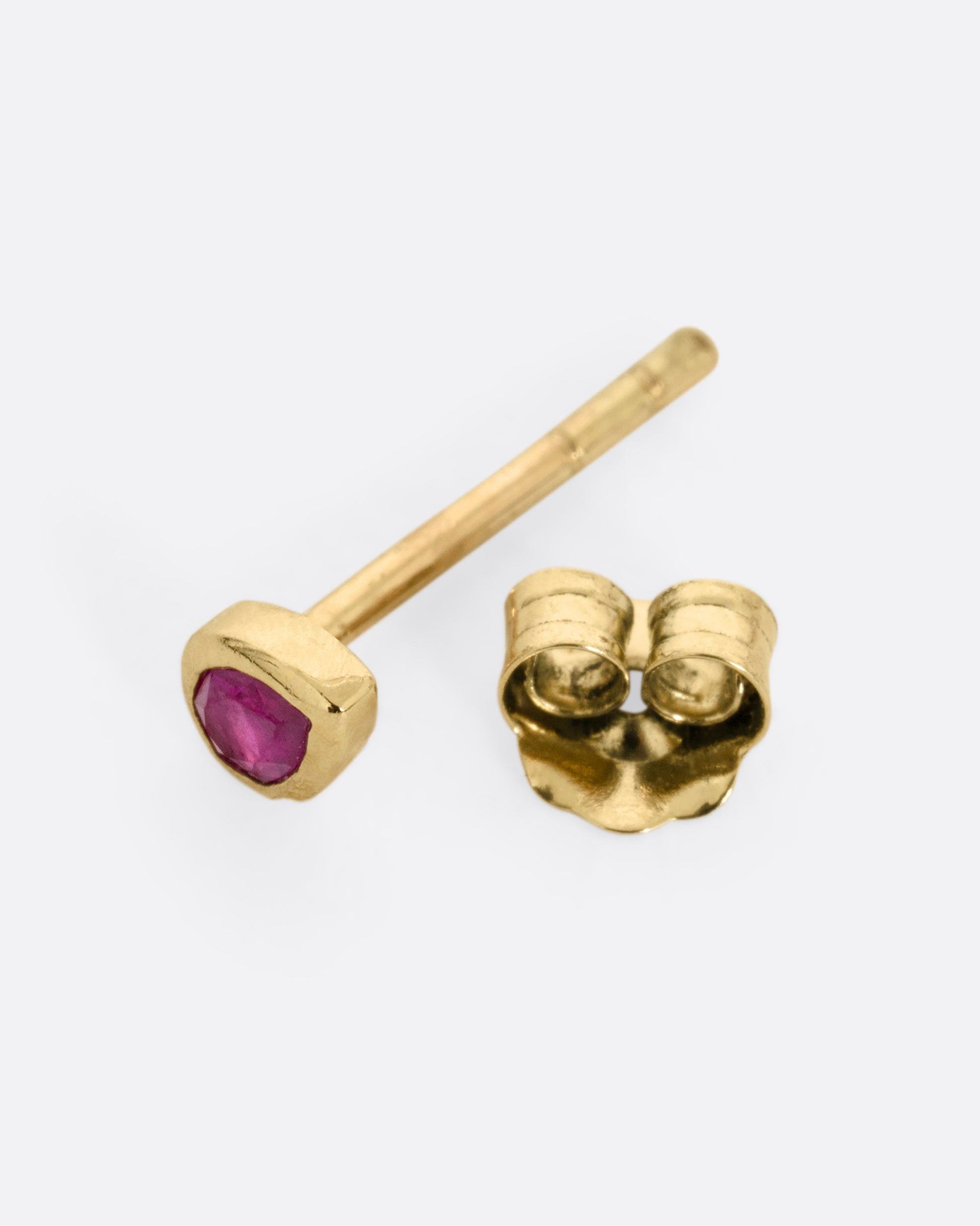 A yellow gold stud earring with a pear shaped ruby, shown open from the side.