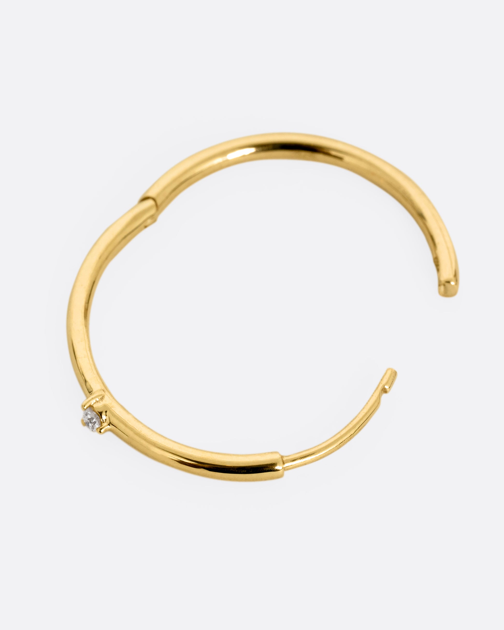 A yellow gold hoop earring with a tiny prong set diamond, shown open from the side.