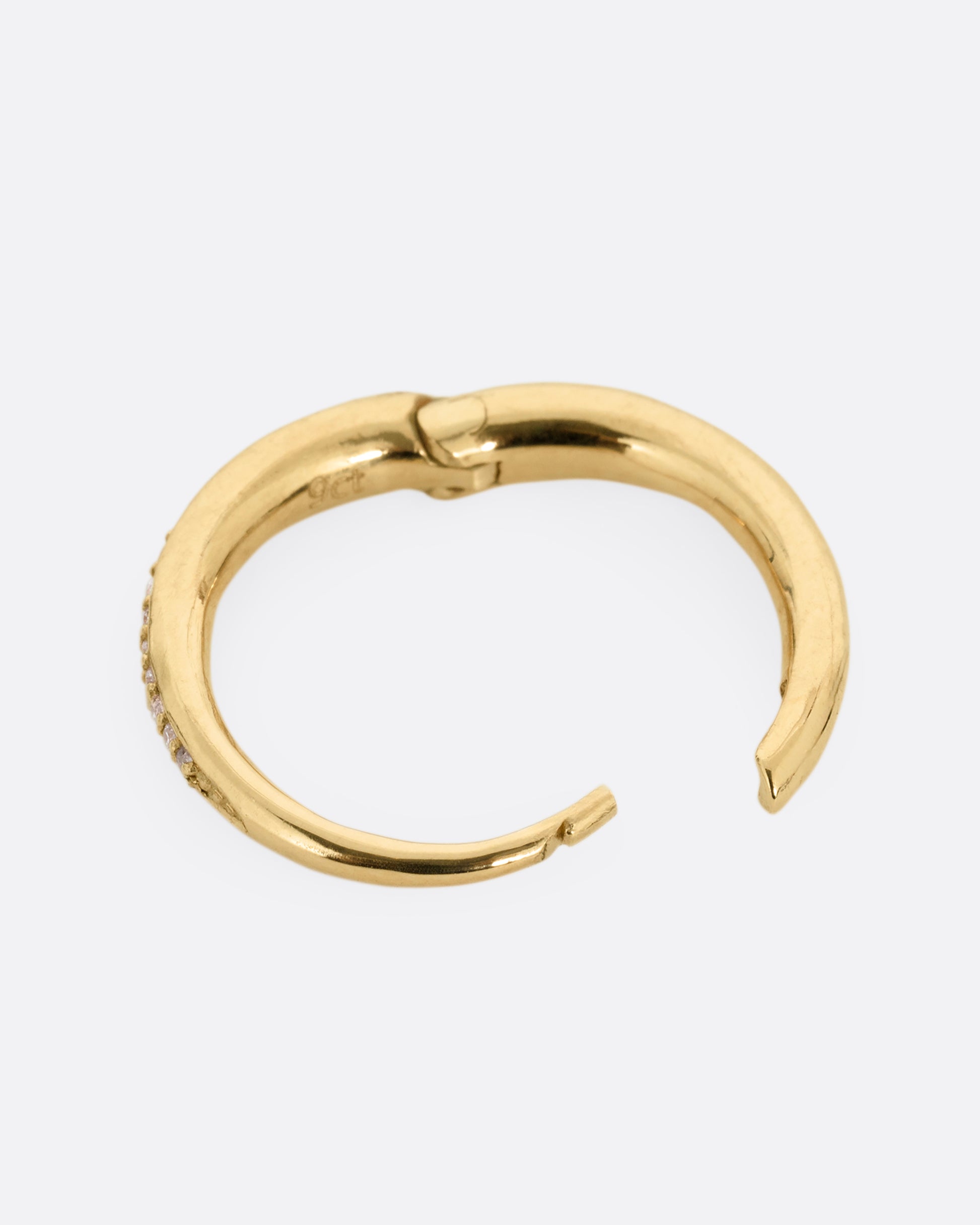 A yellow gold tapered hoop with a queue of graduated diamonds. Shown open on its side.