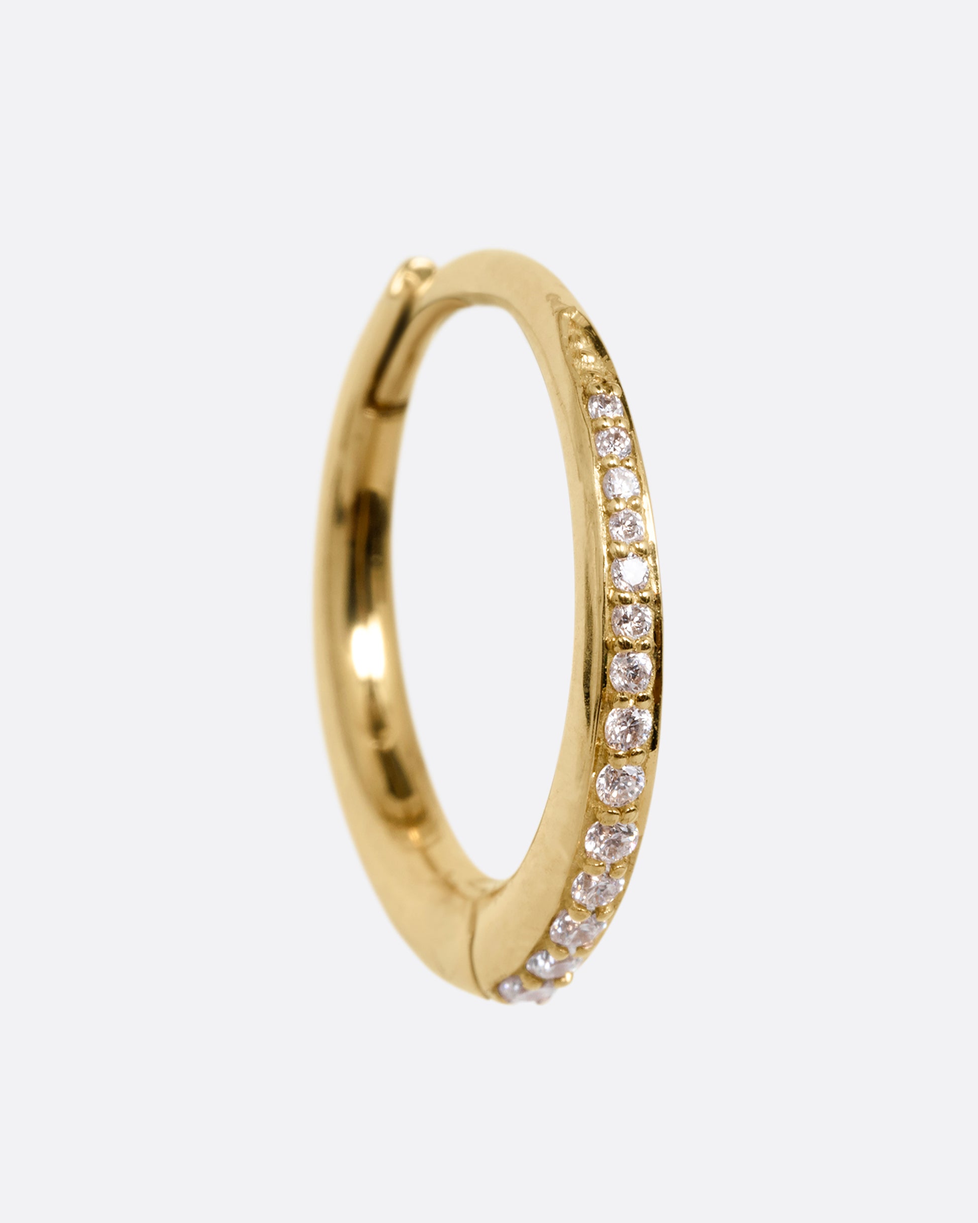 A yellow gold tapered hoop with a queue of graduated diamonds. Shown from the front standing up.