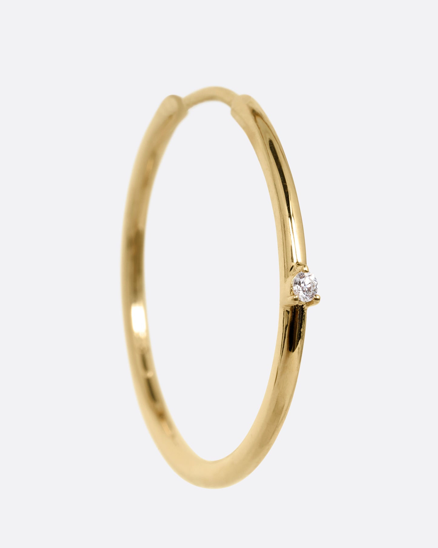 A yellow gold hoop earring with a tiny prong set diamond, shown from the front.