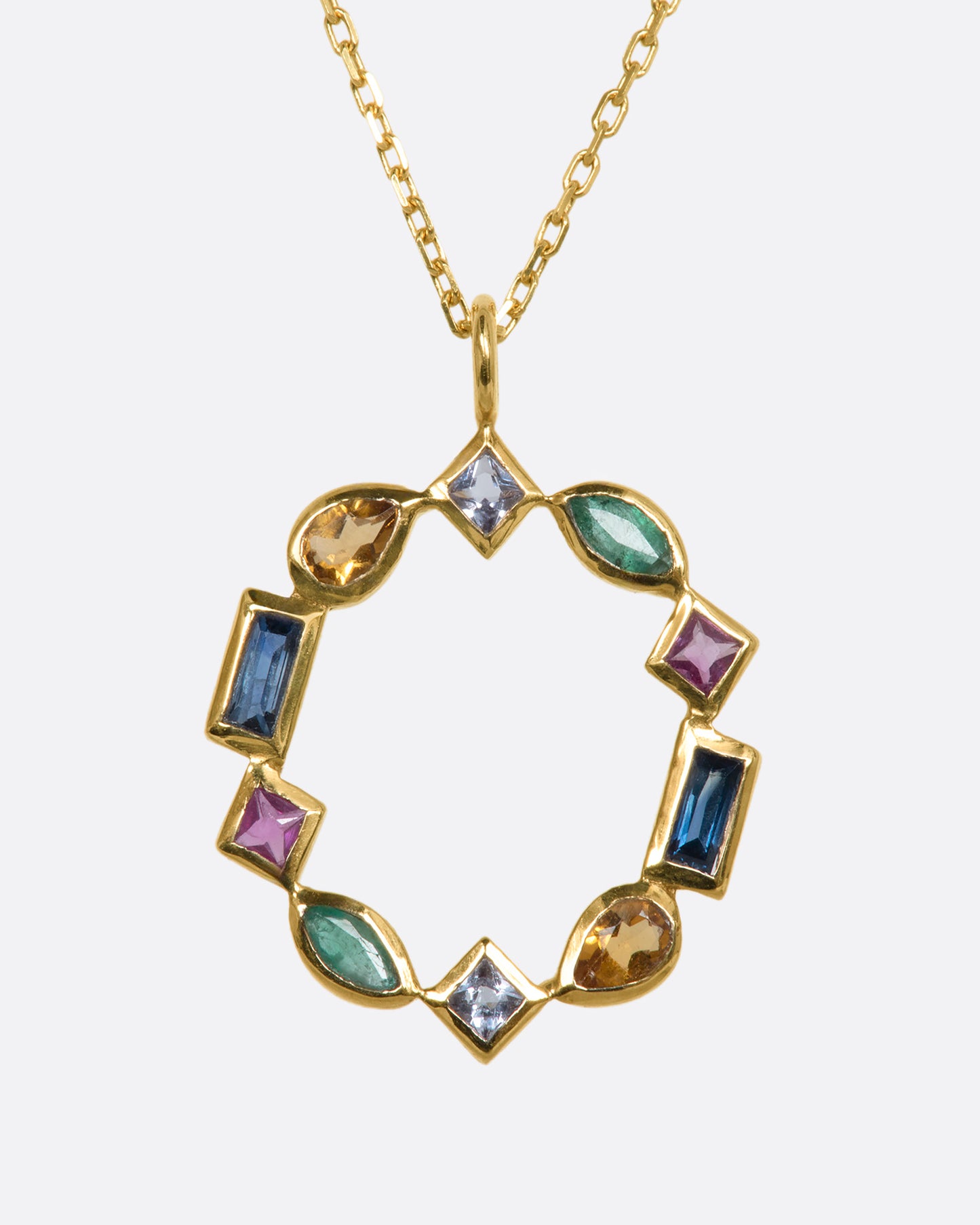 An open circular yellow gold pendant with emeralds, rubies, sapphires, tanzanite, and citrine in varied shaped. Shown from the front.