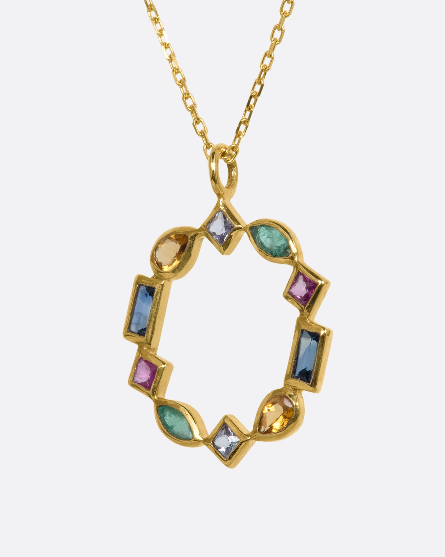 An open circular yellow gold pendant made of emeralds, rubies, sapphires, tanzanite, and citrine in varied shapes. Shown from the side.