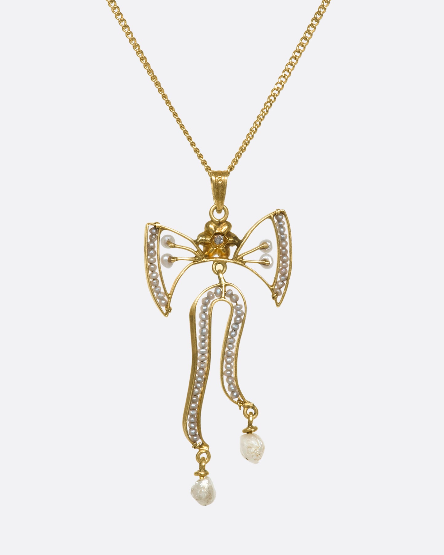 A view of a the backside of a hanging yellow gold bow pendant with seed pearls and a diamond with some of the chain showing.